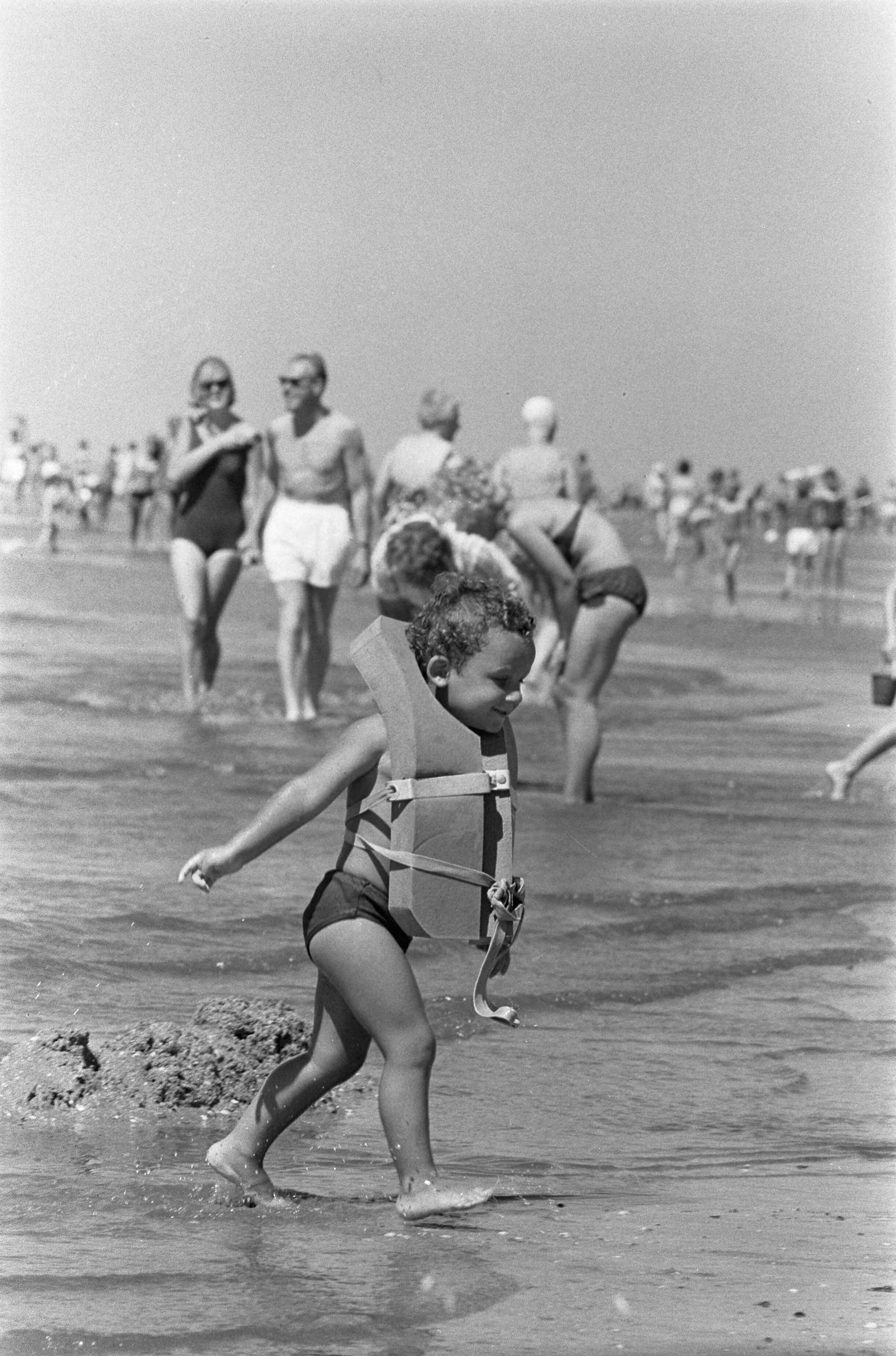 Fotocollectie Anefo — Drukte aan de kust. Strand van Zandvoort. Met een groot zwemvest komt Mikky uit het water — Foto: Pot, Harry / Anefo. Licentie: Set B: Rechtenvrij / Publiek Domein. Bron: Nationaal Archief. http://hdl.handle.net/10648/aa3f5892-d0b4-102d-bcf8-003048976d84