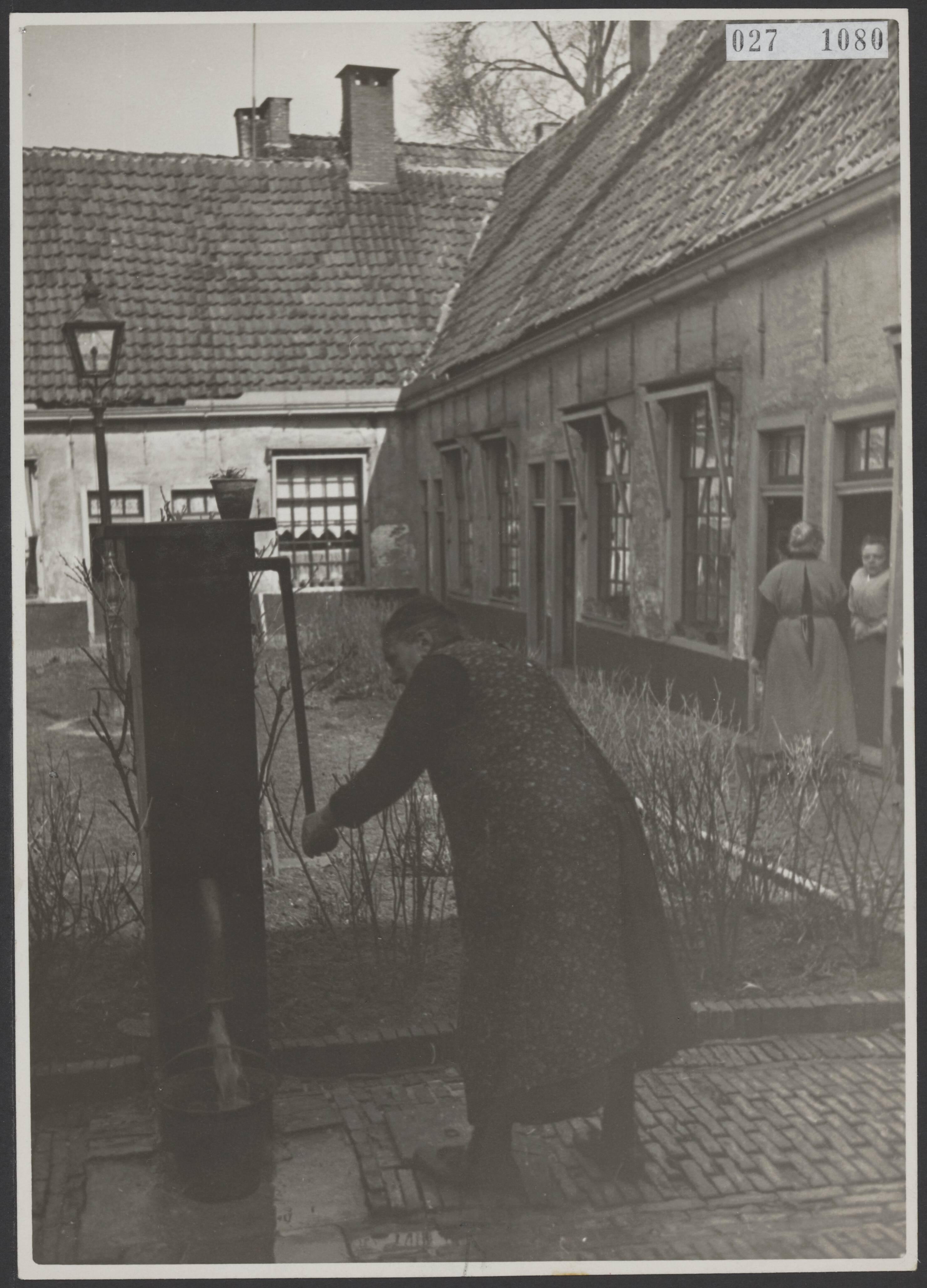 Fotocollectie Elsevier Binnenland — Vrouw pompt water in oud hofje bij de Grote Kerk te Leeuwarden — Foto: Onbekend / Publiek Domein of Rechtenvrij. Licentie: Set B: Rechtenvrij / Publiek Domein. Bron: Nationaal Archief. http://hdl.handle.net/10648/addb9056-d0b4-102d-bcf8-003048976d84