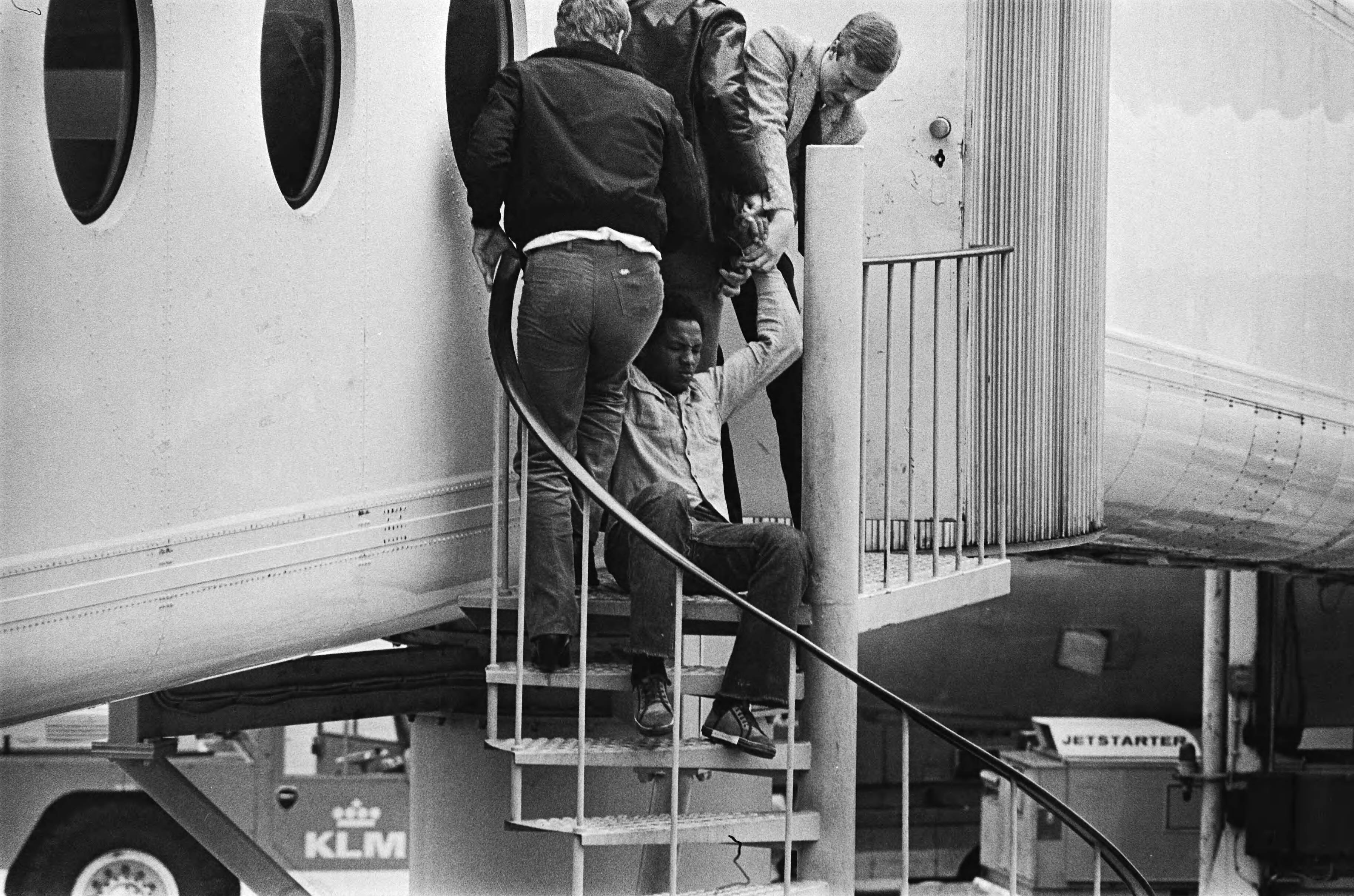 Uitzetting op Schiphol van 8 illegale immigranten naar Marokko — Een van van de mannen verzet zich hevig en wordt een trap opgehesen — Foto: Bogaerts, Rob / Anefo. Licentie: Set B: Rechtenvrij / Publiek Domein. Bron: Nationaal Archief. http://hdl.handle.net/10648/ace445d0-d0b4-102d-bcf8-003048976d84