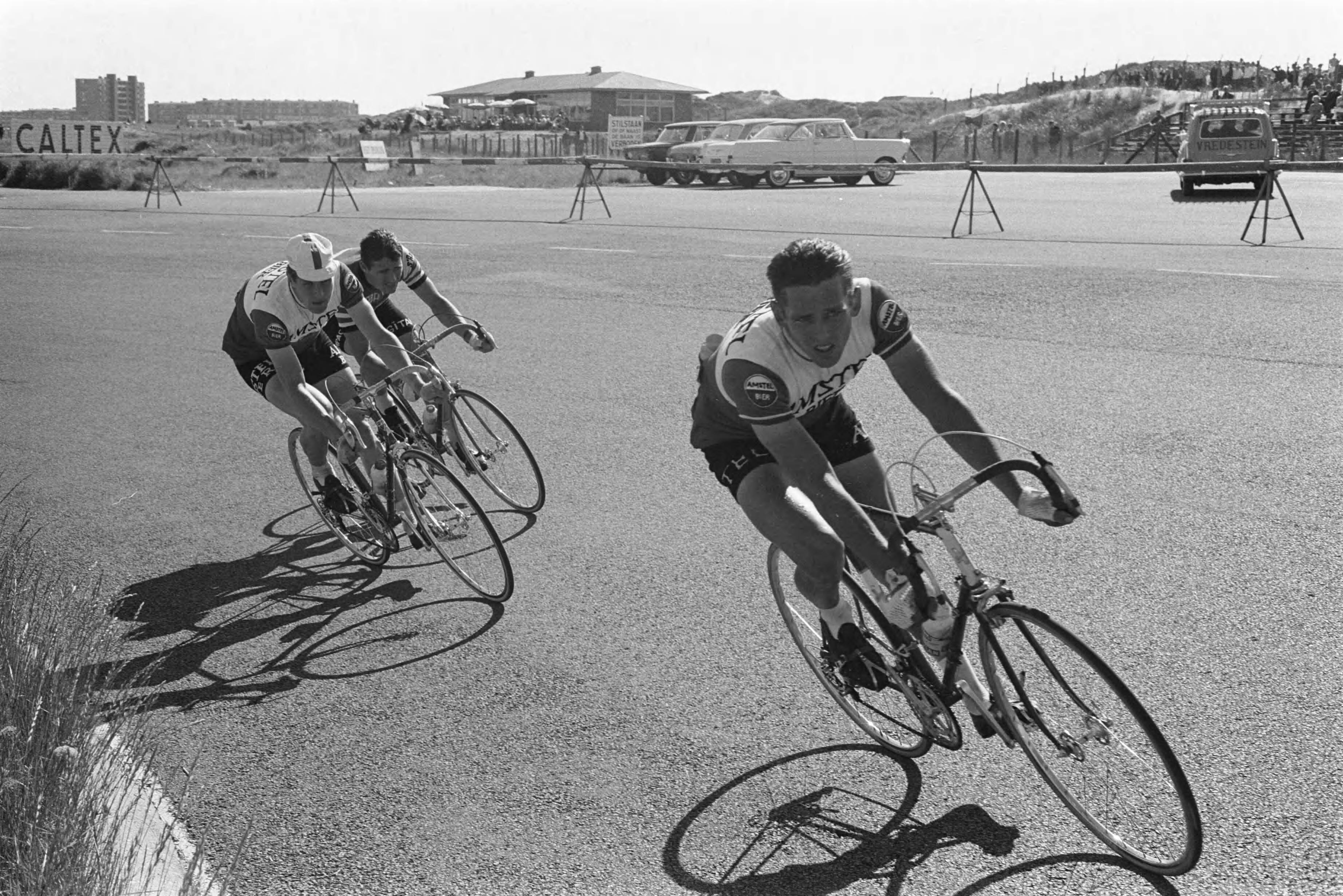 NK Wielrennen 1963 — Nederlands kampioenschap wielrennen op de weg op Circuit Zandvoort. Drie professionals in de bocht, voorop Dick Groeneweg, achter hem Peter Post (Amstel), de lagere winnaar en Ab Geldermans — Foto: Pot, Harry / Anefo. Licentie: Set B: Rechtenvrij / Publiek Domein. Bron: Nationaal Archief. http://hdl.handle.net/10648/aa3f3448-d0b4-102d-bcf8-003048976d84