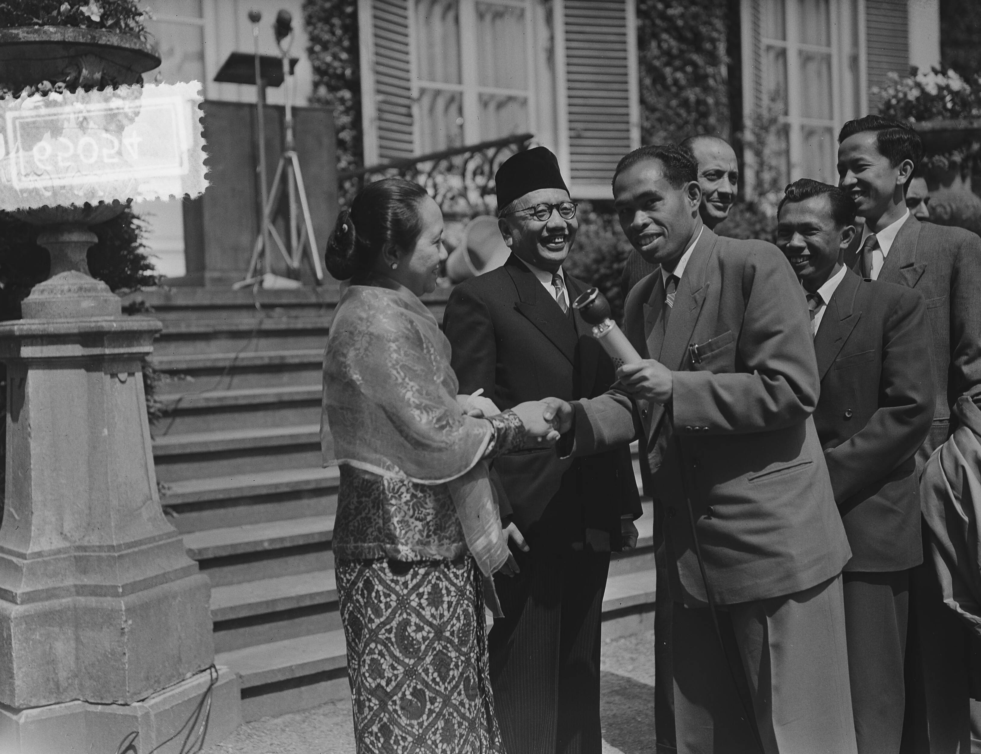 Fotocollectie Anefo — Viering van islamitisch feest Lebaran in de ambtswoning van de Hoge Commissaris van Indonesië, dr. Sutanto Tirtoprojo, te Wassenaar. Een Indonesische radioverslaggever schudt de hand van mevr. Sutanto. Tussen hen in een lachende dr. Sutanto — Foto: Bilsen, Joop van / Anefo. Licentie: Set B: Rechtenvrij / Publiek Domein. Bron: Nationaal Archief. http://hdl.handle.net/10648/a9232786-d0b4-102d-bcf8-003048976d84