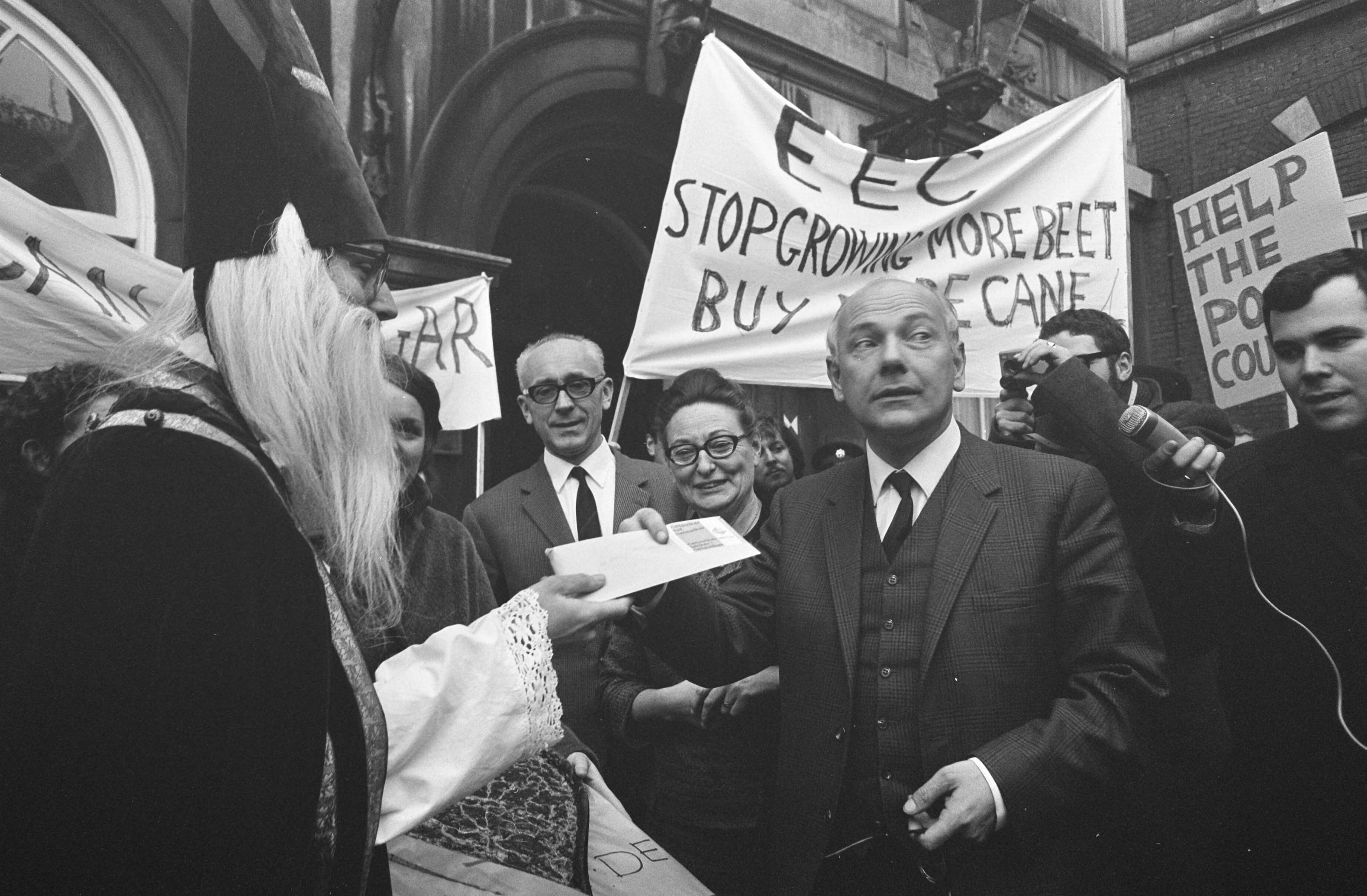 Fotocollectie Anefo — Rietsuikeractie 1968 de demonstranten op het Binnenhof Den Uyl krijgt zakje met rietsuiker — Foto: Kroon, Ron / Anefo. Licentie: Set B: Rechtenvrij / Publiek Domein. Bron: Nationaal Archief. http://hdl.handle.net/10648/ab56c3fa-d0b4-102d-bcf8-003048976d84