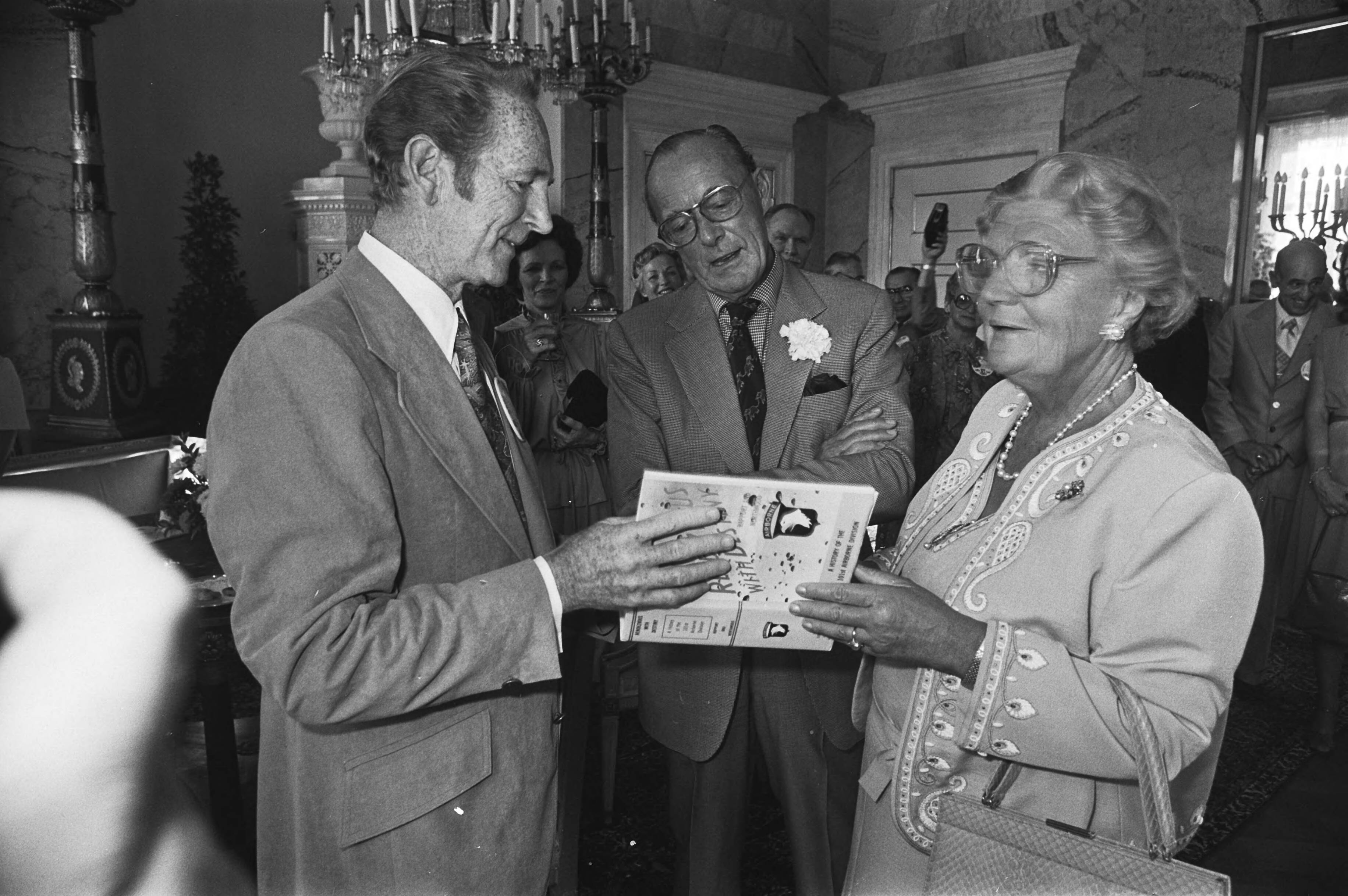 Boek over de 101e Airborne Division door oudstrijders aan koningin Juliana aangeboden op Paleis Soestdijk — De president van de 101st Airborne Division Association, Weldon Combs, overhandigt een boek over deze divisie aan koningin Juliana, terwijl prins Bernhard toekijkt — Foto: Suyk, Koen / Anefo. Licentie: Set B: Rechtenvrij / Publiek Domein. Bron: Nationaal Archief. http://hdl.handle.net/10648/acd14cbe-d0b4-102d-bcf8-003048976d84