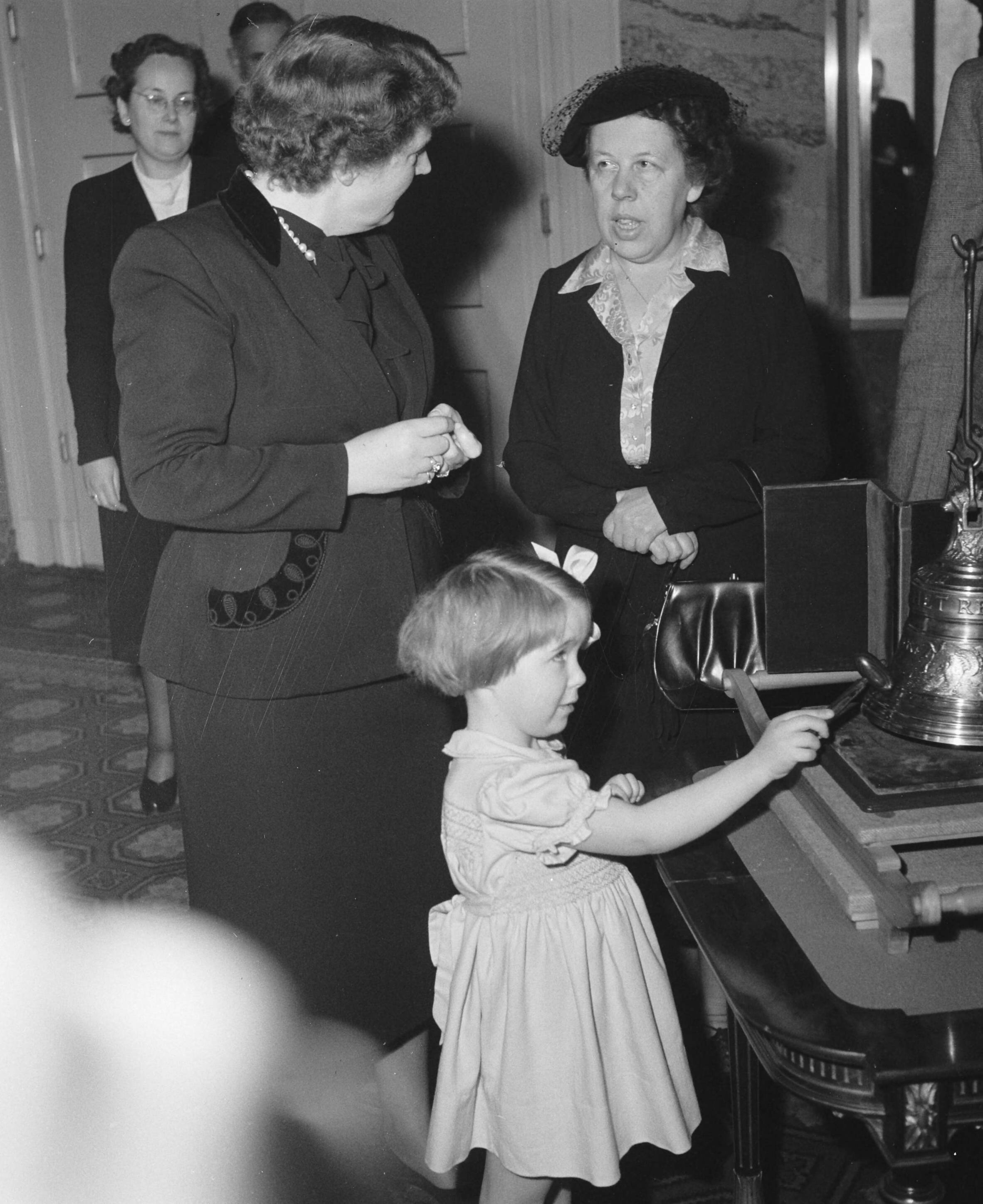 Aanbieding op paleis Soestdijk aan prinses Christina van de kleinste luidklok, het z.g. Marijke-klokje, behorend tot het carillon dat Nederland als dank aan de Verenigde Staten zal geven — Prinses Marijke (Christina) slaat tegen het klokje; koningin Juliana is in gesprek met Freule Wttewaal van Stoetwegen — Foto: Noske, J.D. / Anefo. Licentie: Set B: Rechtenvrij / Publiek Domein. Bron: Nationaal Archief. http://hdl.handle.net/10648/a8f596b8-d0b4-102d-bcf8-003048976d84