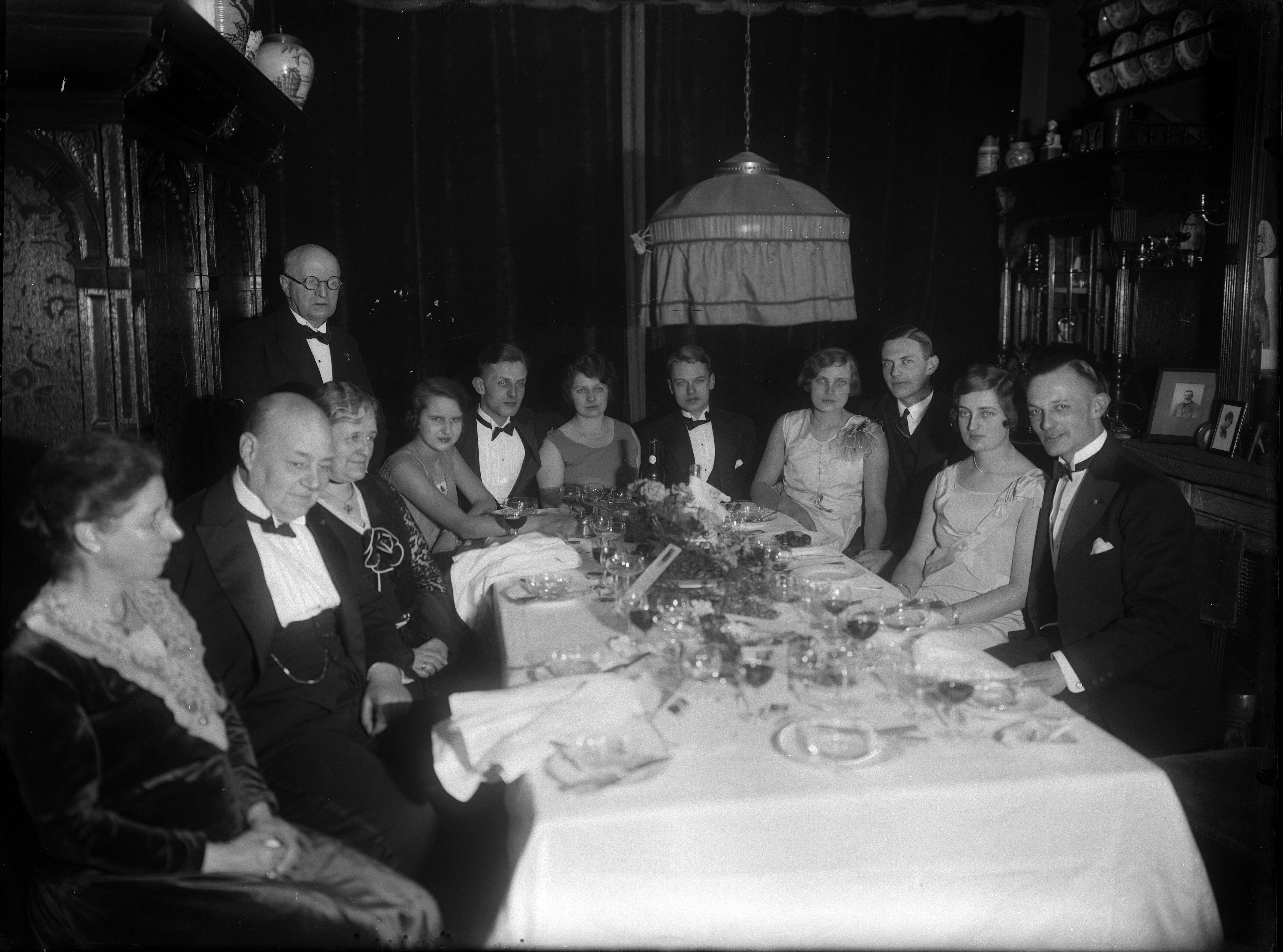 Berg, van den (BERG 050) — Feesten. Een opname van een familie, ouders, dochters en zonen met hun partners, zittend aan een gedekte tafel ter ere van een feestelijke gebeurtenis. Nederland. 1918-1930. 9091 Swaving Dijkstra gravure — Foto: Berg, Th.C.J. van den / Spaarnestad Photo (05887). Licentie: Set B: Rechtenvrij / Publiek Domein. Bron: Nationaal Archief. http://hdl.handle.net/10648/35429da7-c777-a382-e063-6df0900a6686