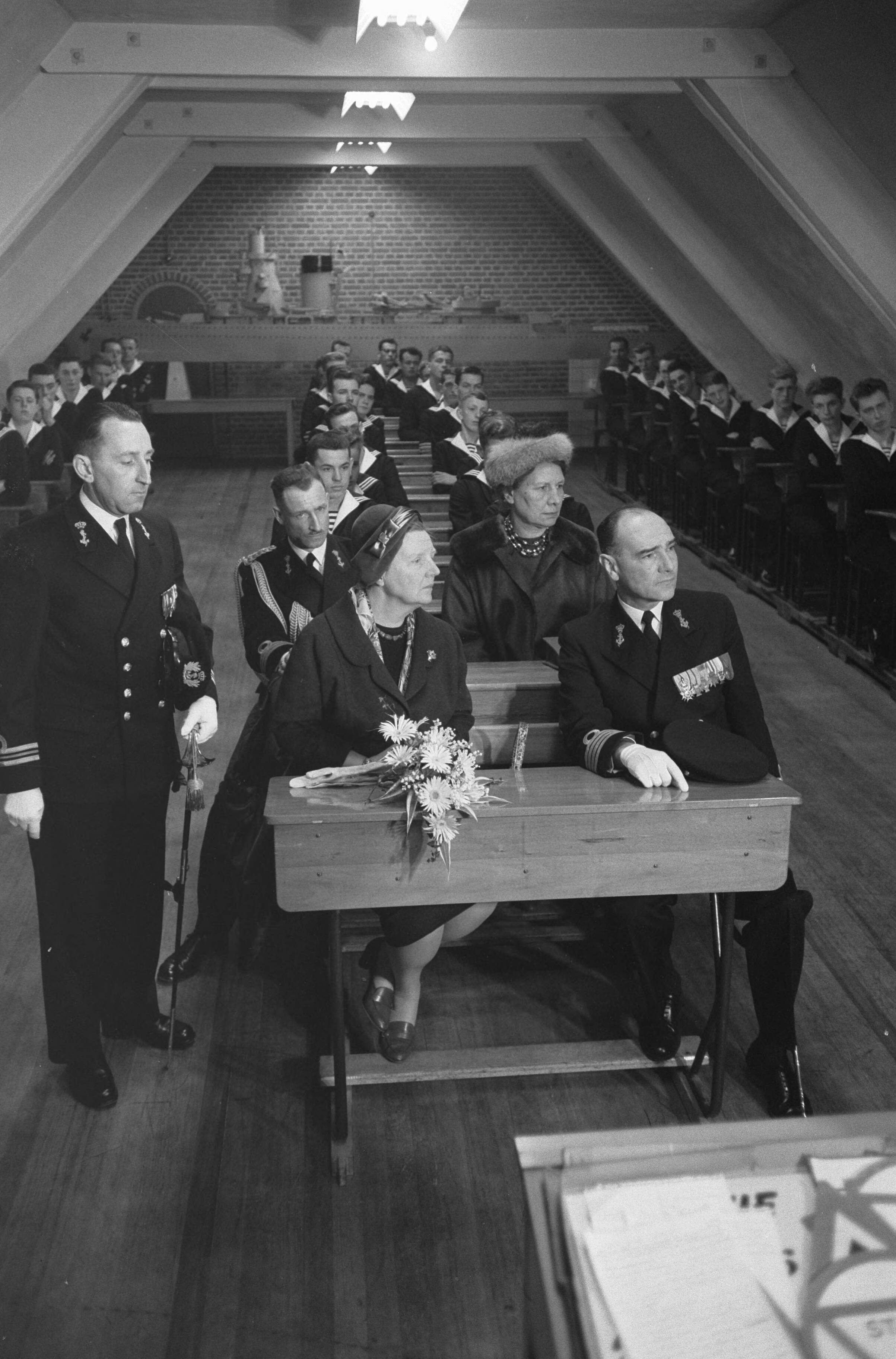 Fotocollectie Anefo — Koningin Juliana bezoekt marinekamp Loosdrecht. De koningin volgt een les over het verkeer in een schoolbank met rechts naast haar de commandant van het opleidingscentrum kapitein-ter-zee H.J. Baay — Foto: Pot, Harry / Anefo. Licentie: Set B: Rechtenvrij / Publiek Domein. Bron: Nationaal Archief. http://hdl.handle.net/10648/a9ce391e-d0b4-102d-bcf8-003048976d84