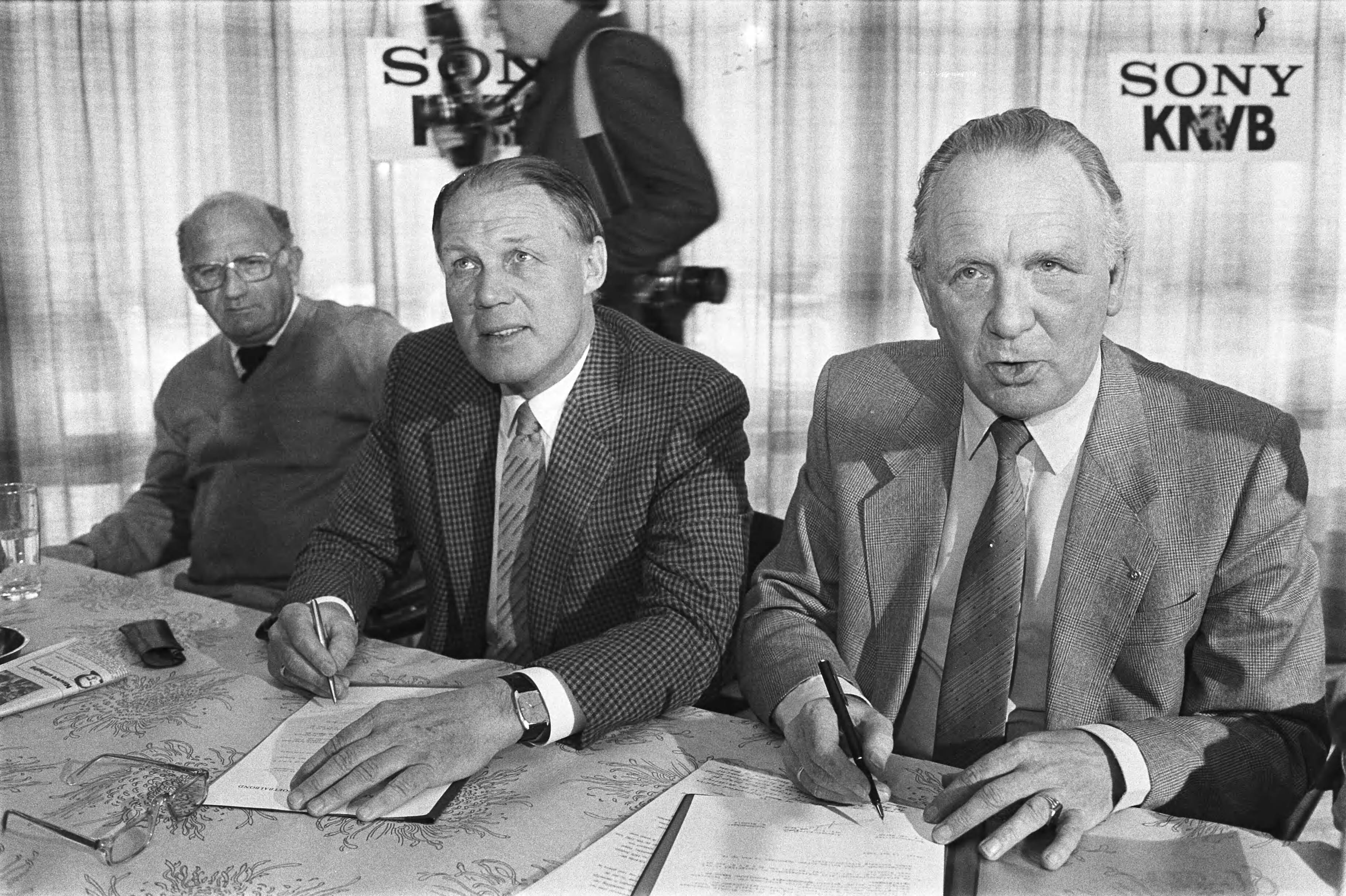 Fotocollectie Anefo — Zeist, Rinus Michels tekent contract voor technisch coordinator bij de KNVB; Rinus Michels tekent contract, links bondscoach Rijvers, rechts KNVB-voorz. — Foto: Antonisse, Marcel / Anefo. Licentie: Set B: Rechtenvrij / Publiek Domein. Bron: Nationaal Archief. http://hdl.handle.net/10648/ad38b4bc-d0b4-102d-bcf8-003048976d84