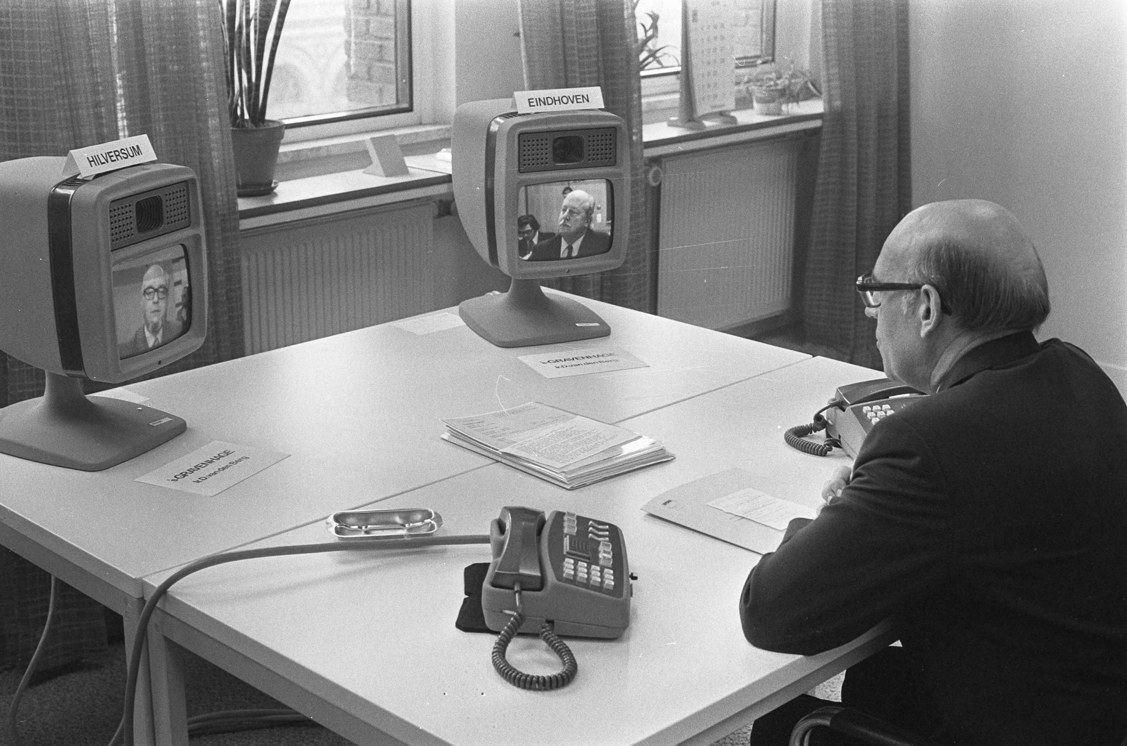 Demonstratie van de beeldtelefoon in Den Haag — Ir. D. van den Berg , (hoofddirecteur technische zaken van de PTT) tijdens de demonstratie in gesprek met Ir. F.Leopold, wetenschappelijk medewerker van Philips (rechts) en Ir. L.J.W. van Loon, projectleider beeldtelefonie van de PTT (links) — Foto: Fotograaf Onbekend / Anefo. Licentie: Set B: Rechtenvrij / Publiek Domein. Bron: Nationaal Archief. http://hdl.handle.net/10648/ac454d04-d0b4-102d-bcf8-003048976d84