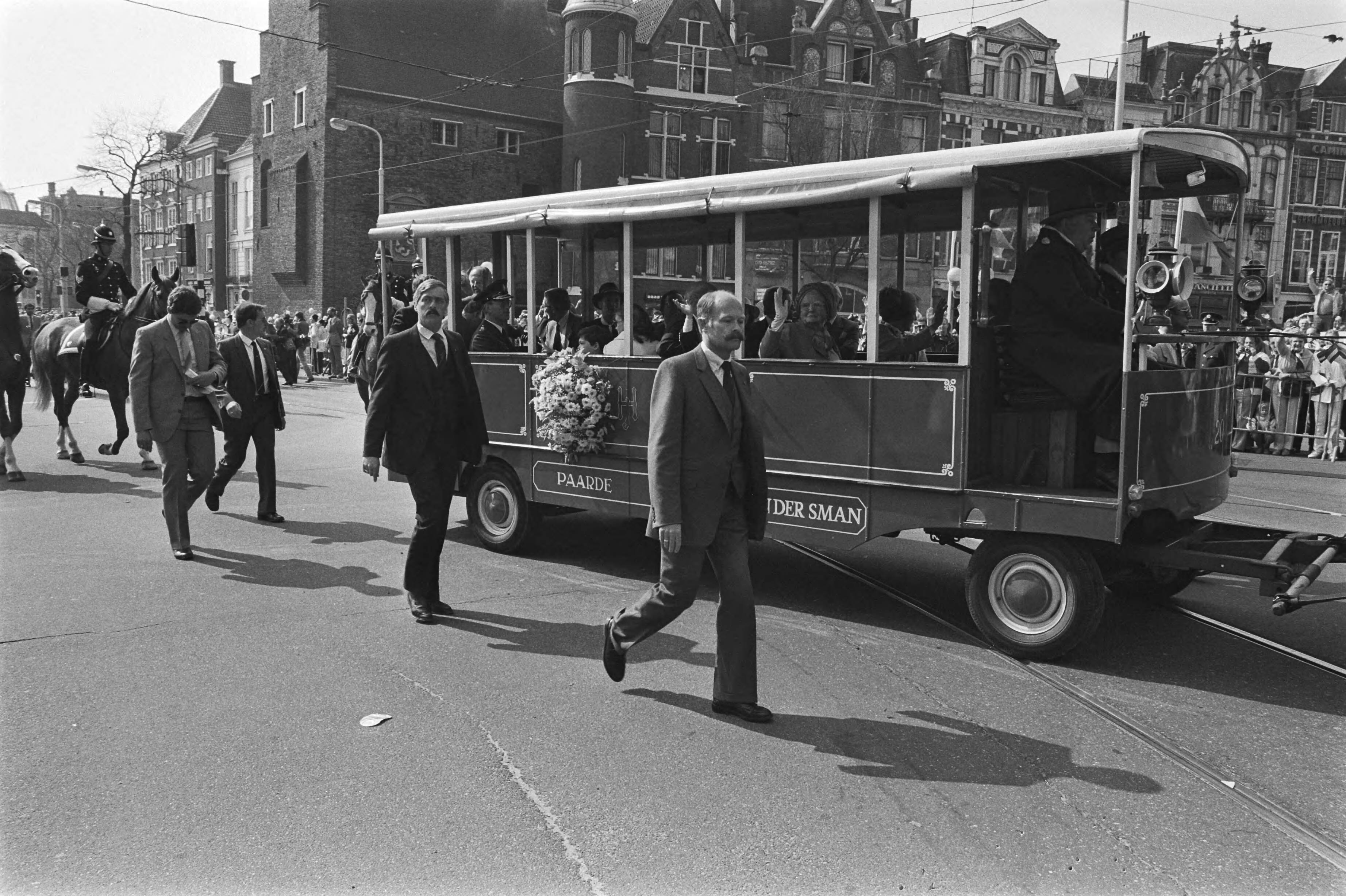 Fotocollectie Anefo — Koninginnedag 1984 in Den Haag ; veiligheidsmensen naast de paardentram met Koninklijke familie — Foto: Antonisse, Marcel / Anefo. Licentie: Set B: Rechtenvrij / Publiek Domein. Bron: Nationaal Archief. http://hdl.handle.net/10648/ad381246-d0b4-102d-bcf8-003048976d84