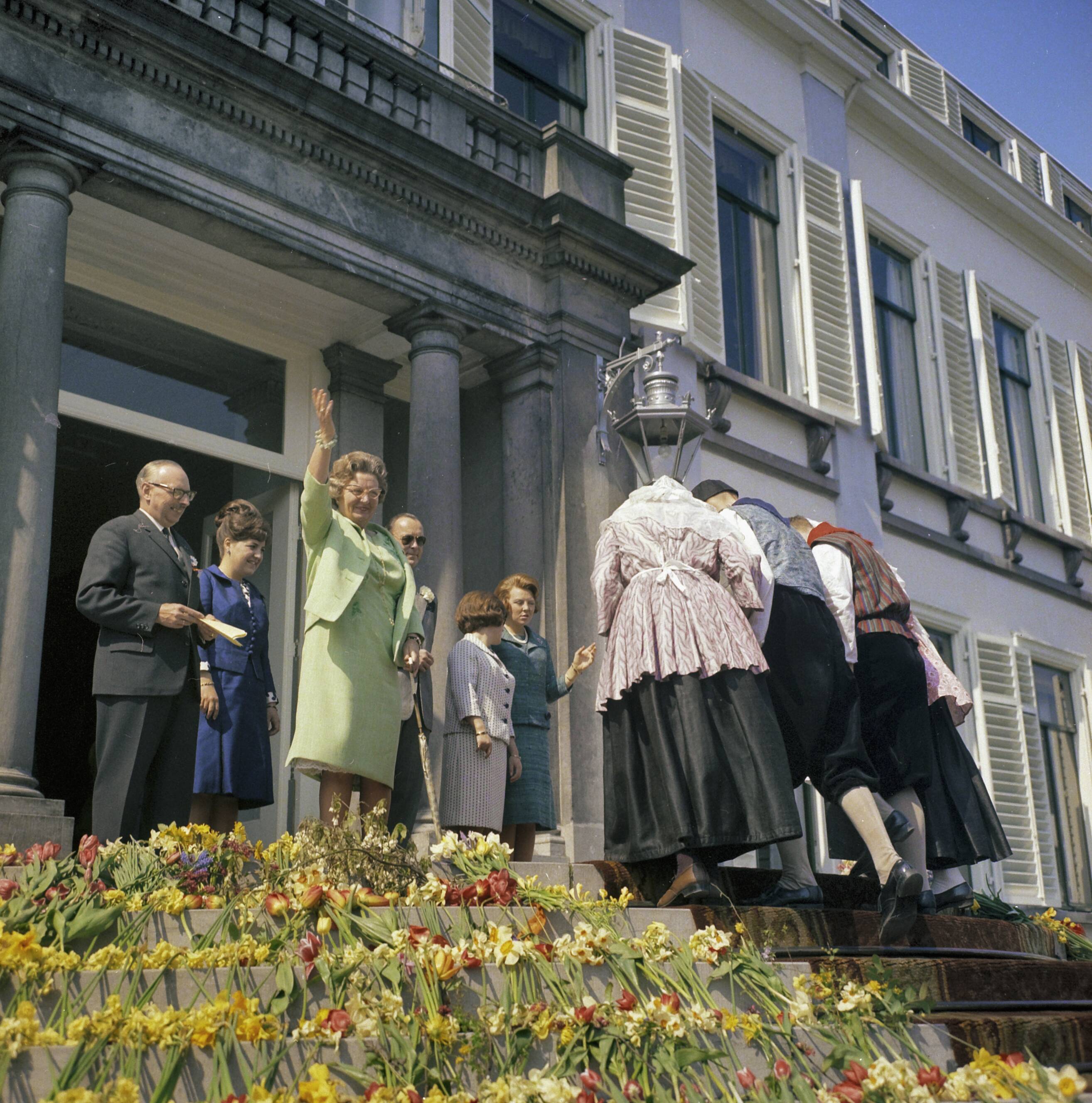 Fotocollectie Anefo — Koninginnedag 1965. Defilé Soestdijk. Konining Juliana zwaait. Vier personen in klederdracht lopen licht gebogen achteruit de trappen af — Foto: Fotograaf Onbekend / Anefo. Licentie: Set B: Rechtenvrij / Publiek Domein. Bron: Nationaal Archief. http://hdl.handle.net/10648/ad8d6836-d0b4-102d-bcf8-003048976d84