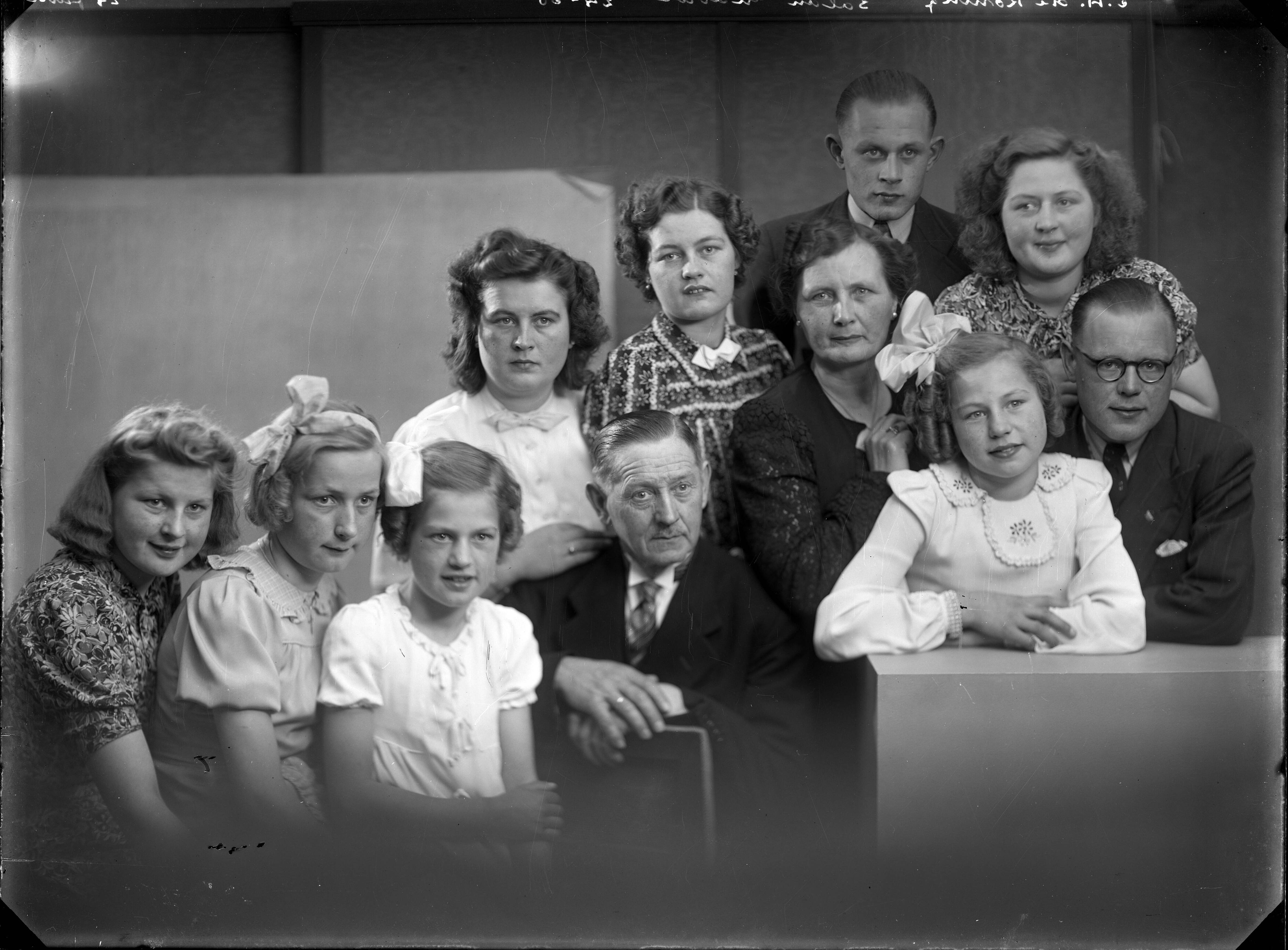 Berg, van den (BERG 050) — Studio-opnames. Een gezin, vader, moeder, hun zeven dochters en hun twee zonen. De meisjes in jurken en strikken in het haar, de jongens in driedelige pakken. Haarlem, Nederland. 1918-1930. E.A. (of C.A.) de Koning salon gravure 24-30 24 juni — Foto: Berg, Th.C.J. van den / Spaarnestad Photo (05887). Licentie: Set B: Rechtenvrij / Publiek Domein. Bron: Nationaal Archief. http://hdl.handle.net/10648/35429da7-c803-a382-e063-6df0900a6686