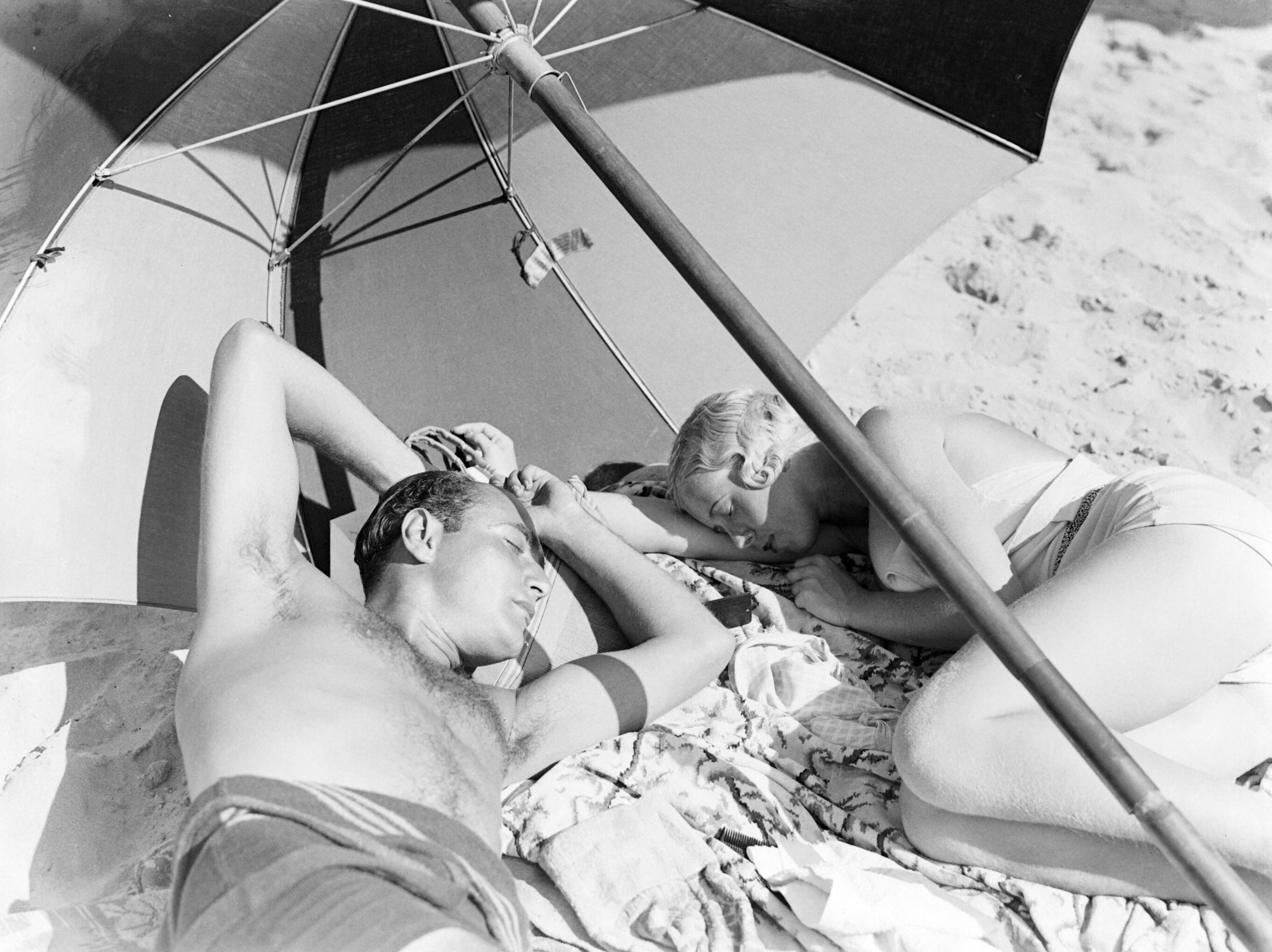 Scheveningen. — Een man (Farrar?) en een vrouw (Yvonne?) onder een parasol op het strand in Scheveningen — Foto: Poll, Willem van de. Licentie: Set B: Rechtenvrij / Publiek Domein. Bron: Nationaal Archief. http://hdl.handle.net/10648/ae9abcba-d0b4-102d-bcf8-003048976d84