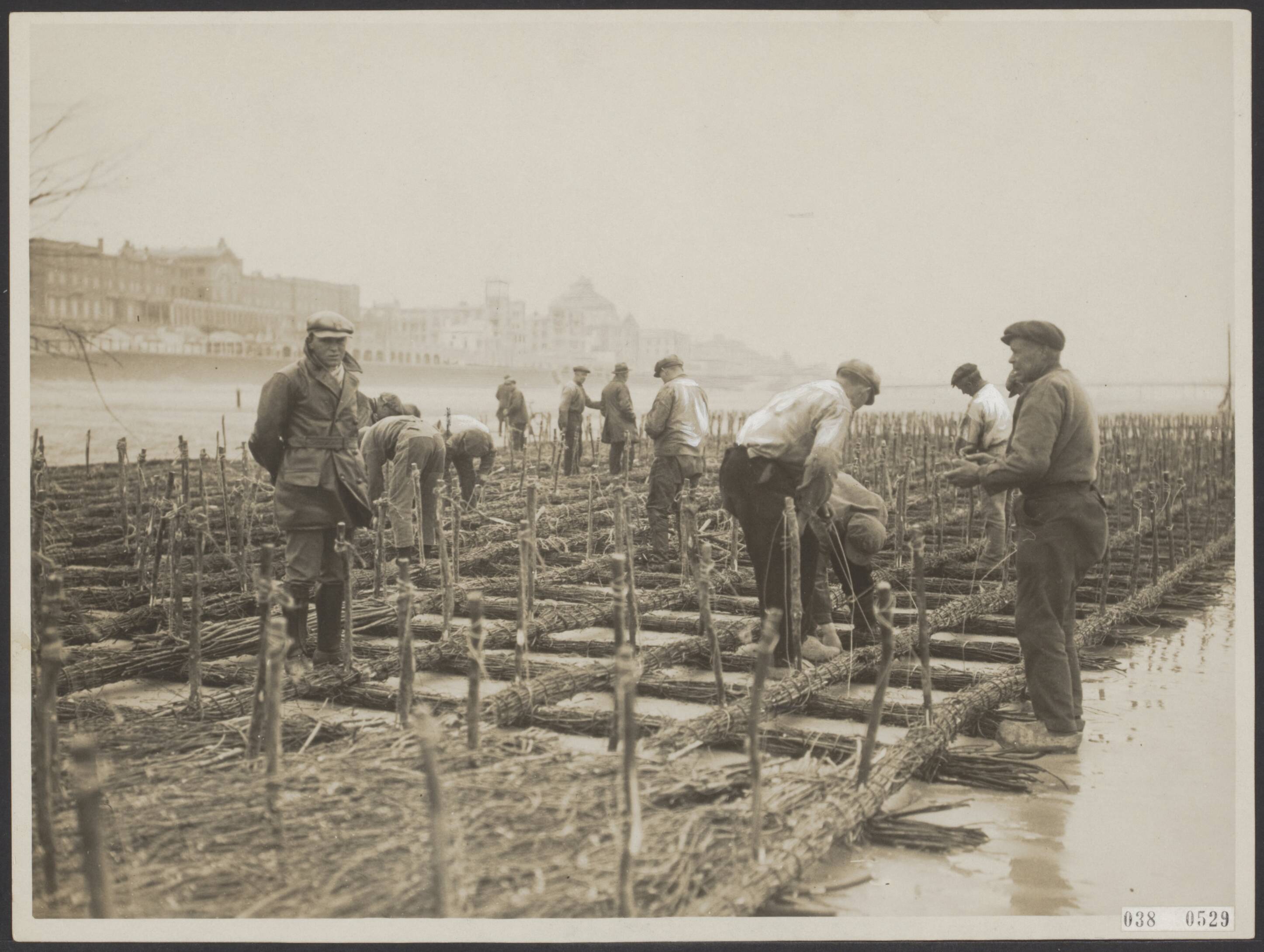 Fotocollectie Elsevier Binnenland — Op het strand van Scheveningen worden van twijgen grote brekers in elkaar gezet. Deze worden, verzwaard met steen en puin, in zee gelaten om de kleine binnenpieren tegen de zware golfslag te beschemen — Foto: N.V. Polygoon. Licentie: Set B: Rechtenvrij / Publiek Domein. Bron: Nationaal Archief. http://hdl.handle.net/10648/adf1da50-d0b4-102d-bcf8-003048976d84
