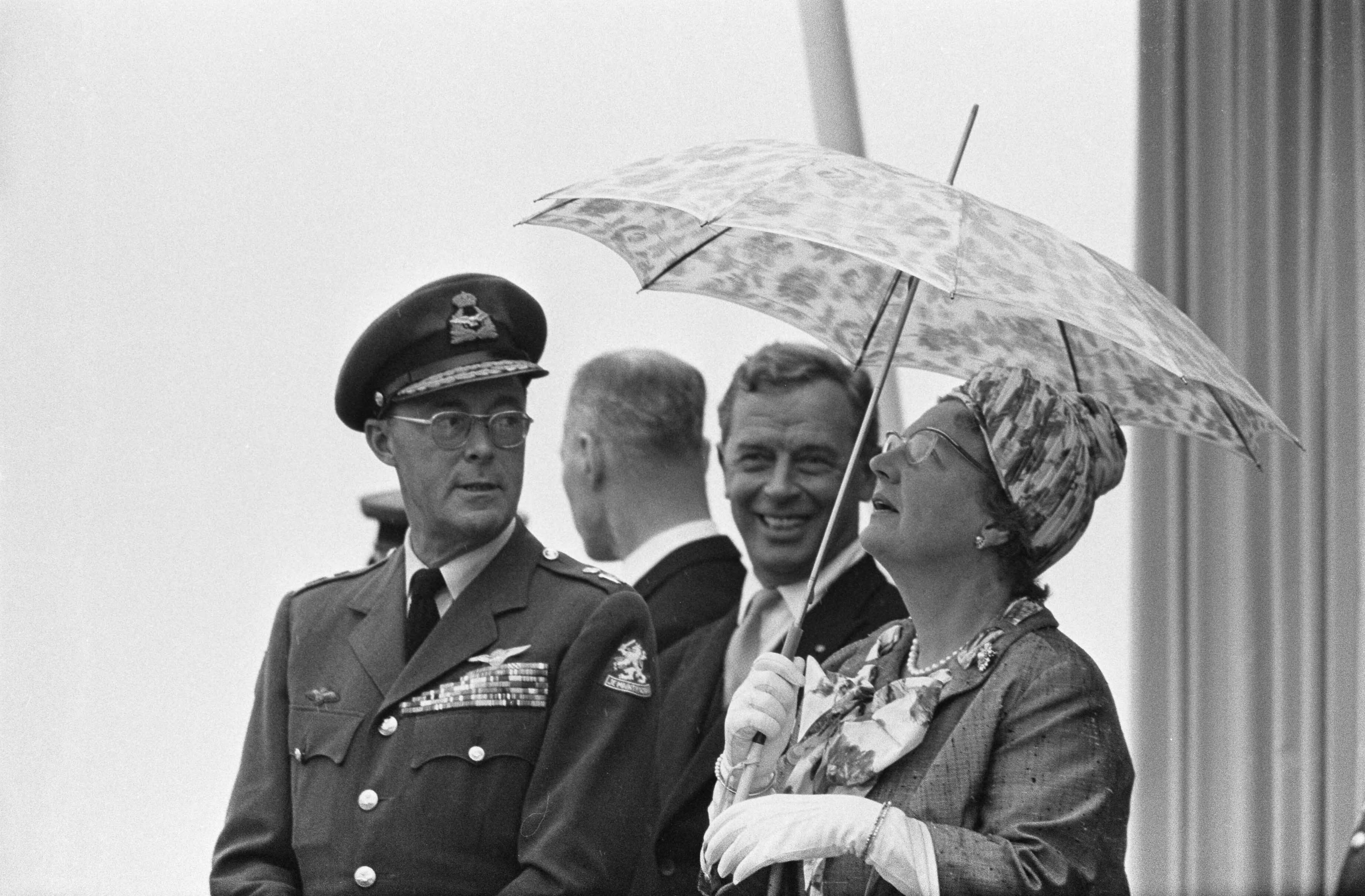 Fotocollectie Anefo — Vijftig jaar Koninklijke Luchtmacht. Defilé op Soesterberg. Koningin Juliana steekt een paraplu op, naast haar prins Bernhard en minister Visser — Foto: Koch, Eric / Anefo. Licentie: Set B: Rechtenvrij / Publiek Domein. Bron: Nationaal Archief. http://hdl.handle.net/10648/aa3d36ac-d0b4-102d-bcf8-003048976d84