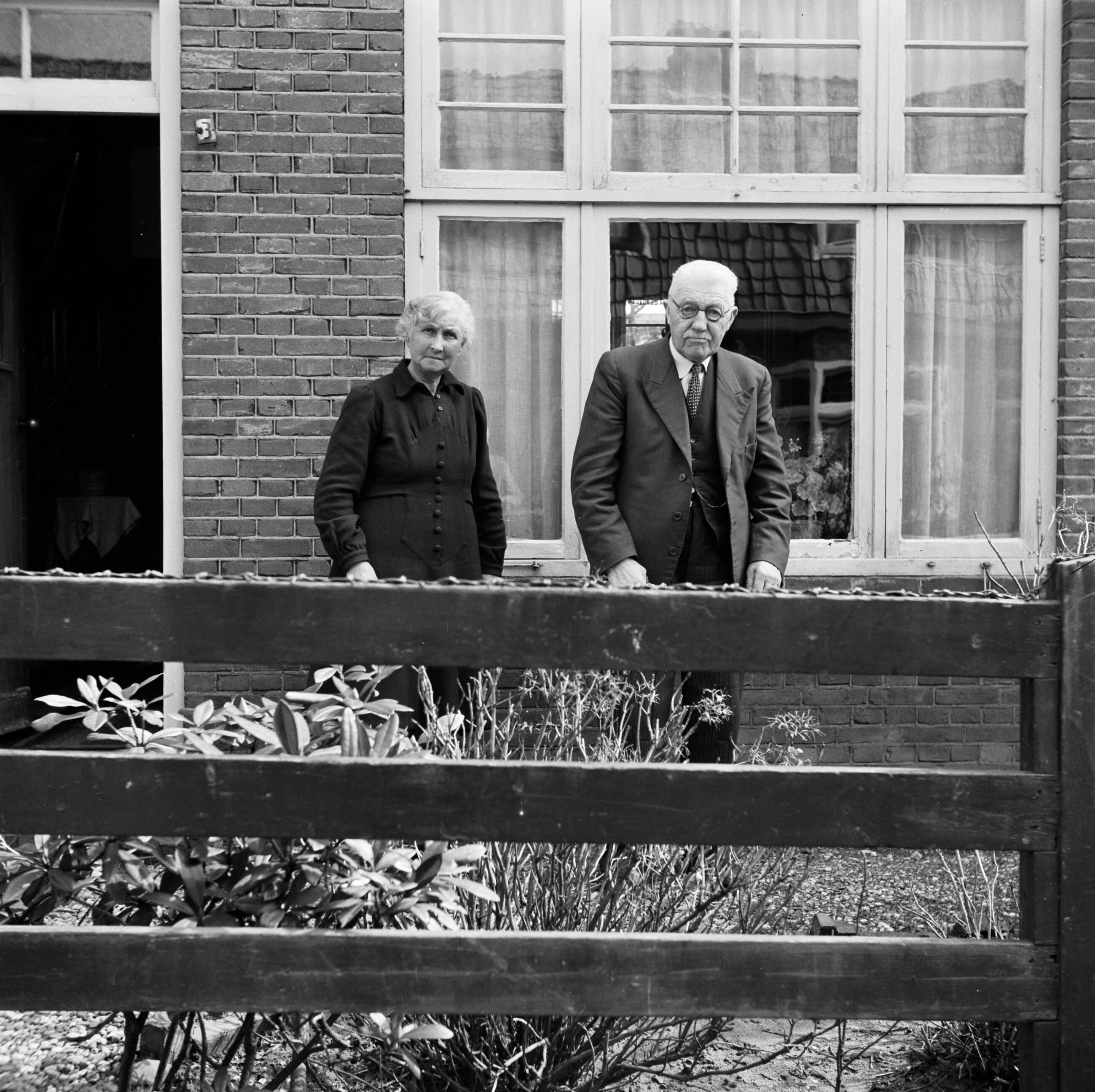 Fotocollectie Van de Poll — Het echtpaar S. de Jong in de tuin voor hun woning in het Friese Huizum (nu deel van Leeuwarden) — Foto: Poll, Willem van de. Licentie: Set B: Rechtenvrij / Publiek Domein. Bron: Nationaal Archief. http://hdl.handle.net/10648/aeccc502-d0b4-102d-bcf8-003048976d84