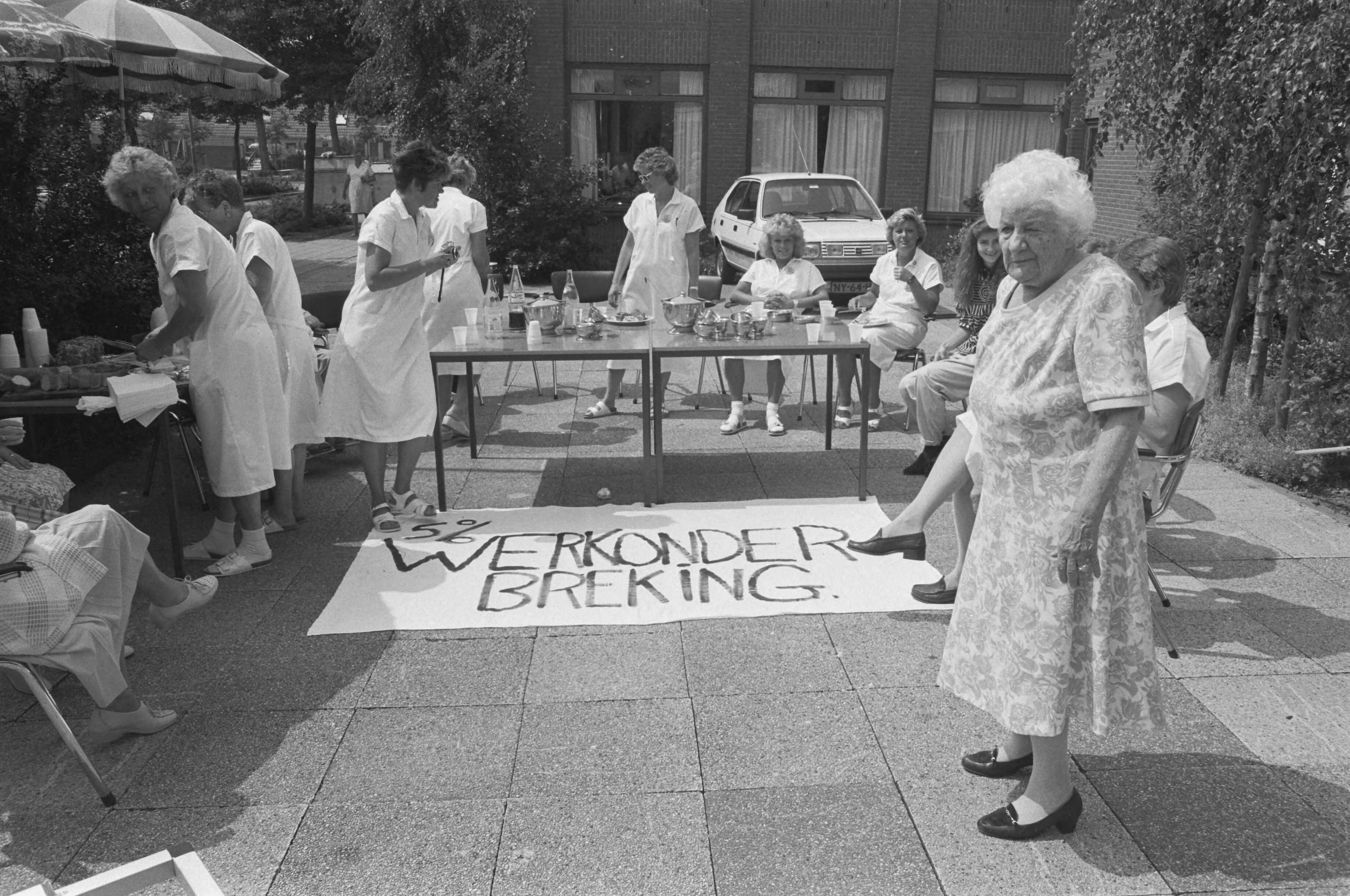 Actie in het bejaardentehuis St. Joseph in Purmerend voor 5% CAO looneis — Verplegend personeel buiten aan de koffie rond een spandoek op de grond — Foto: Croes, Rob C. / Anefo. Licentie: Set B: Rechtenvrij / Publiek Domein. Bron: Nationaal Archief. http://hdl.handle.net/10648/ad73efe6-d0b4-102d-bcf8-003048976d84
