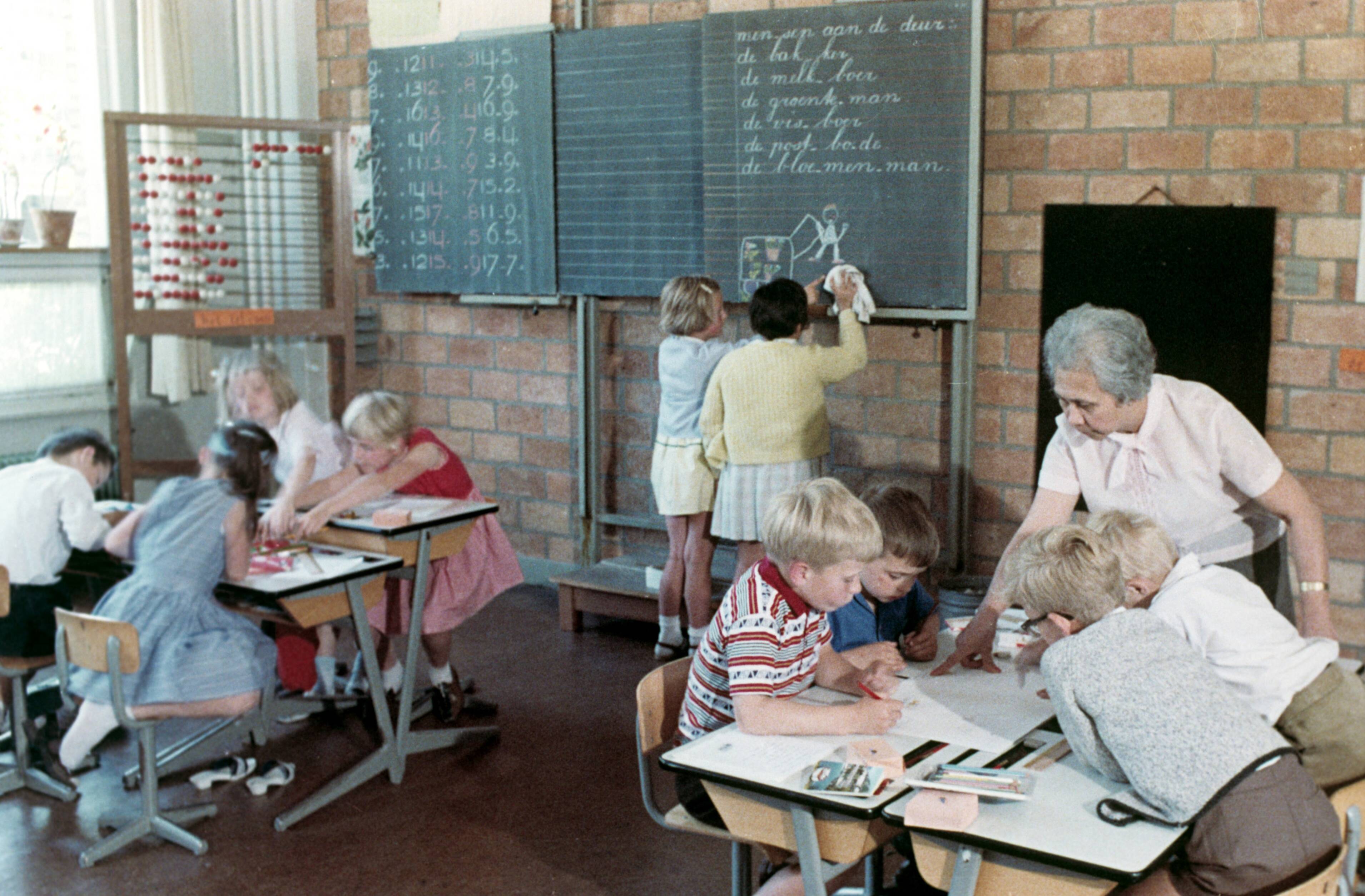 Collectie nader te bepalen — [Schoolklas Lager onderwijs. Links een groot telraam. Twee meisjes maken een tekening op een schoolbord. Rechts geeft een oudere onderwijzeres uitleg bij een groepje van vier scholieren] — Foto: Fotograaf Onbekend / Fotobureau onbekend / Spaarnestad Photo (05887). Licentie: Set B: Rechtenvrij / Publiek Domein. Bron: Nationaal Archief. http://hdl.handle.net/10648/35429da6-38a7-a382-e063-6df0900a6686