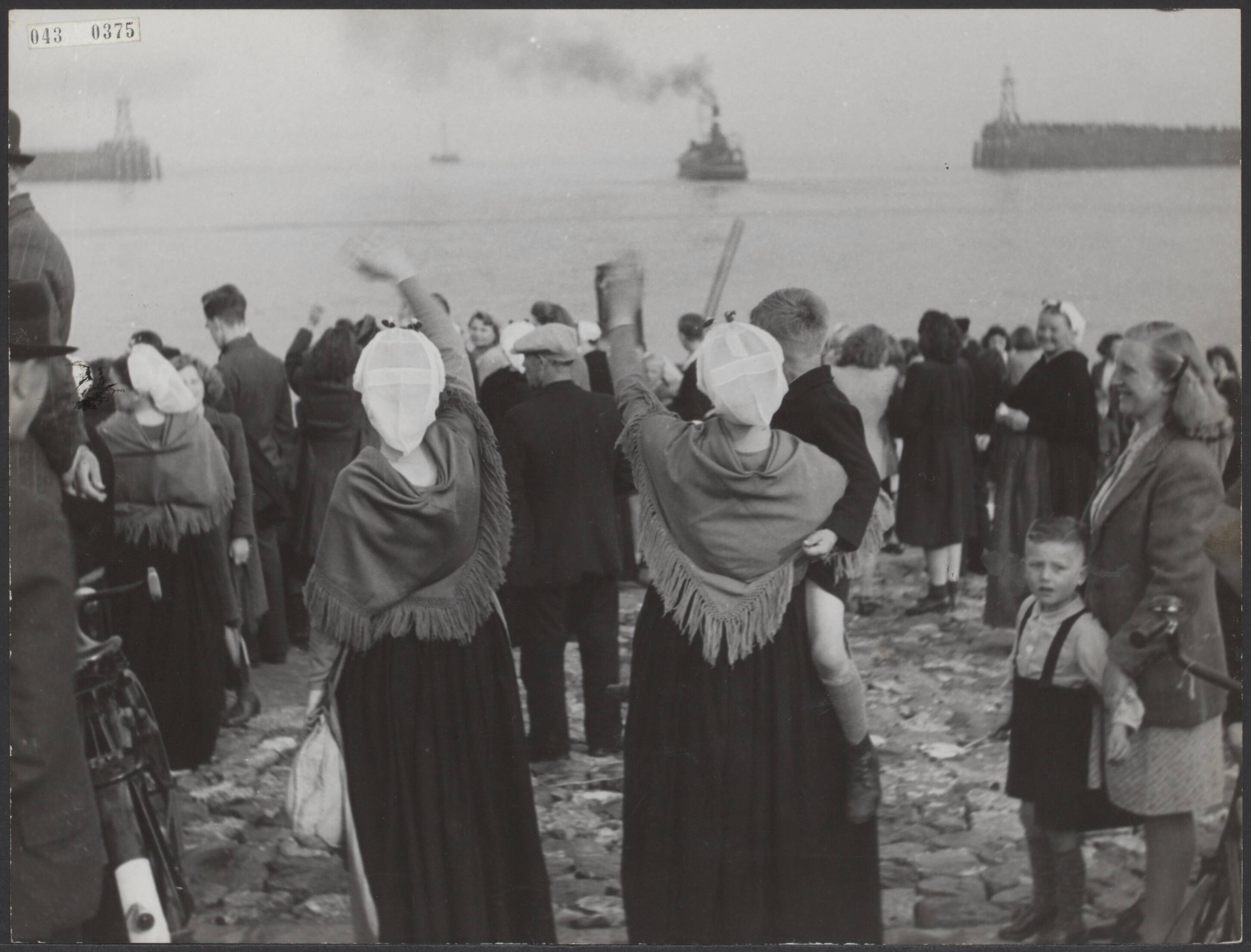 Fotocollectie Elsevier Binnenland — [Publiek, waaronder vrouwen in Scheveningse klederdracht, zwaait vissersschepen uit die de haven van Scheveningen verlaten] — Foto: Associated Correspondents. Licentie: Set B: Rechtenvrij / Publiek Domein. Bron: Nationaal Archief. http://hdl.handle.net/10648/adf8d0bc-d0b4-102d-bcf8-003048976d84