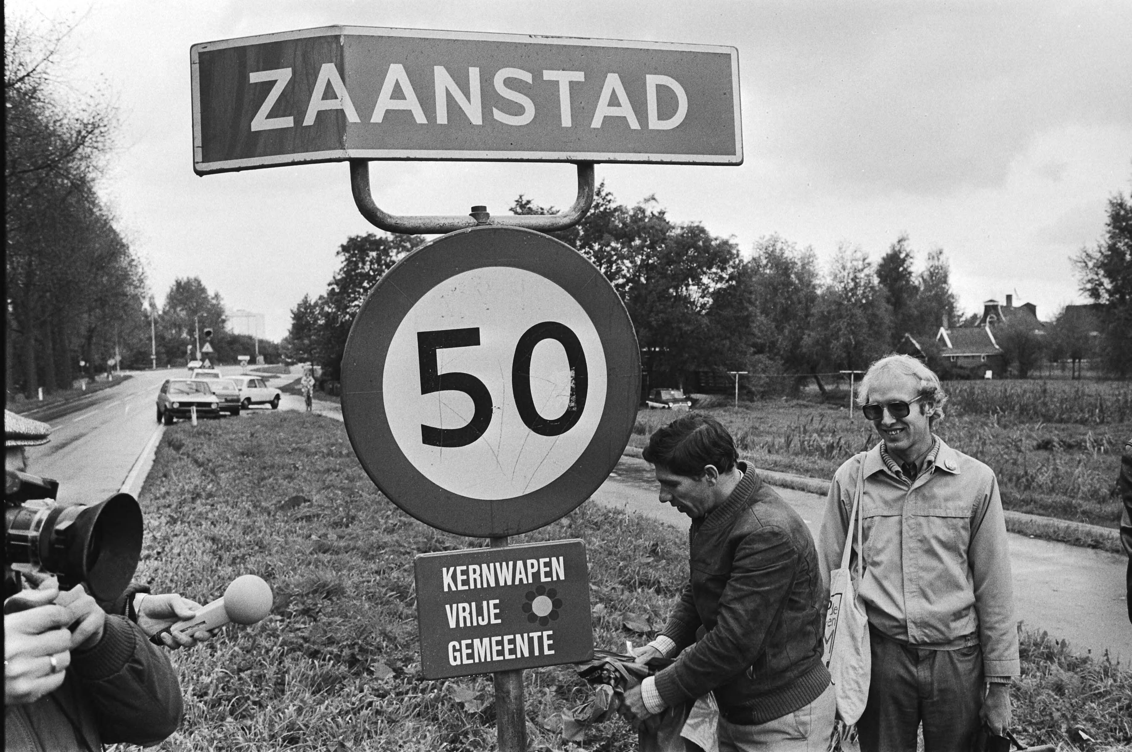 Fotocollectie Anefo — Wethouder Nieuwenhuizen (l) onthult in de gemeente Zaanstad, als 1e gemeente, een bordje "Kernwapenvrije gemeente". Rechts Nico Schouten van het actiecomité Stop de Neutronenbom — Foto: Antonisse, Marcel / Anefo. Licentie: Set B: Rechtenvrij / Publiek Domein. Bron: Nationaal Archief. http://hdl.handle.net/10648/ad200228-d0b4-102d-bcf8-003048976d84