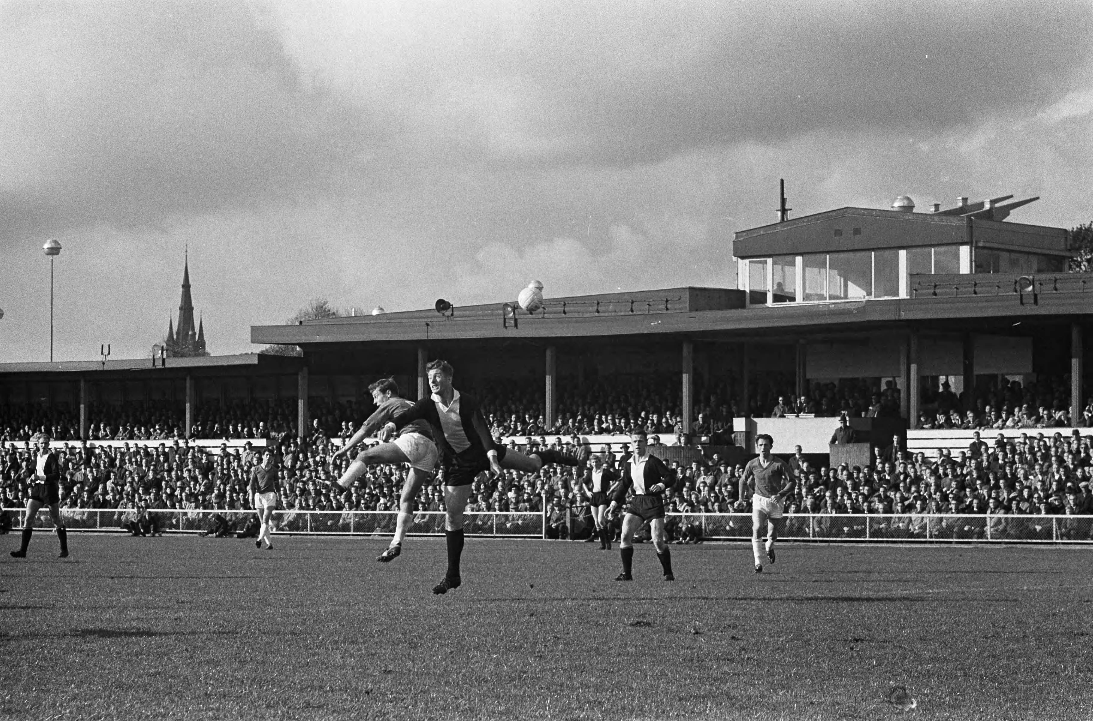 Fotocollectie Anefo — Voetbal. 't Gooi tegen Alkmaar '54 1-1. Spelmoment, De Vries (Alkmaar) in duel met een 't-Gooi verdediger — Foto: Gelderen, Hugo van / Anefo. Licentie: Set B: Rechtenvrij / Publiek Domein. Bron: Nationaal Archief. http://hdl.handle.net/10648/aa4953b0-d0b4-102d-bcf8-003048976d84