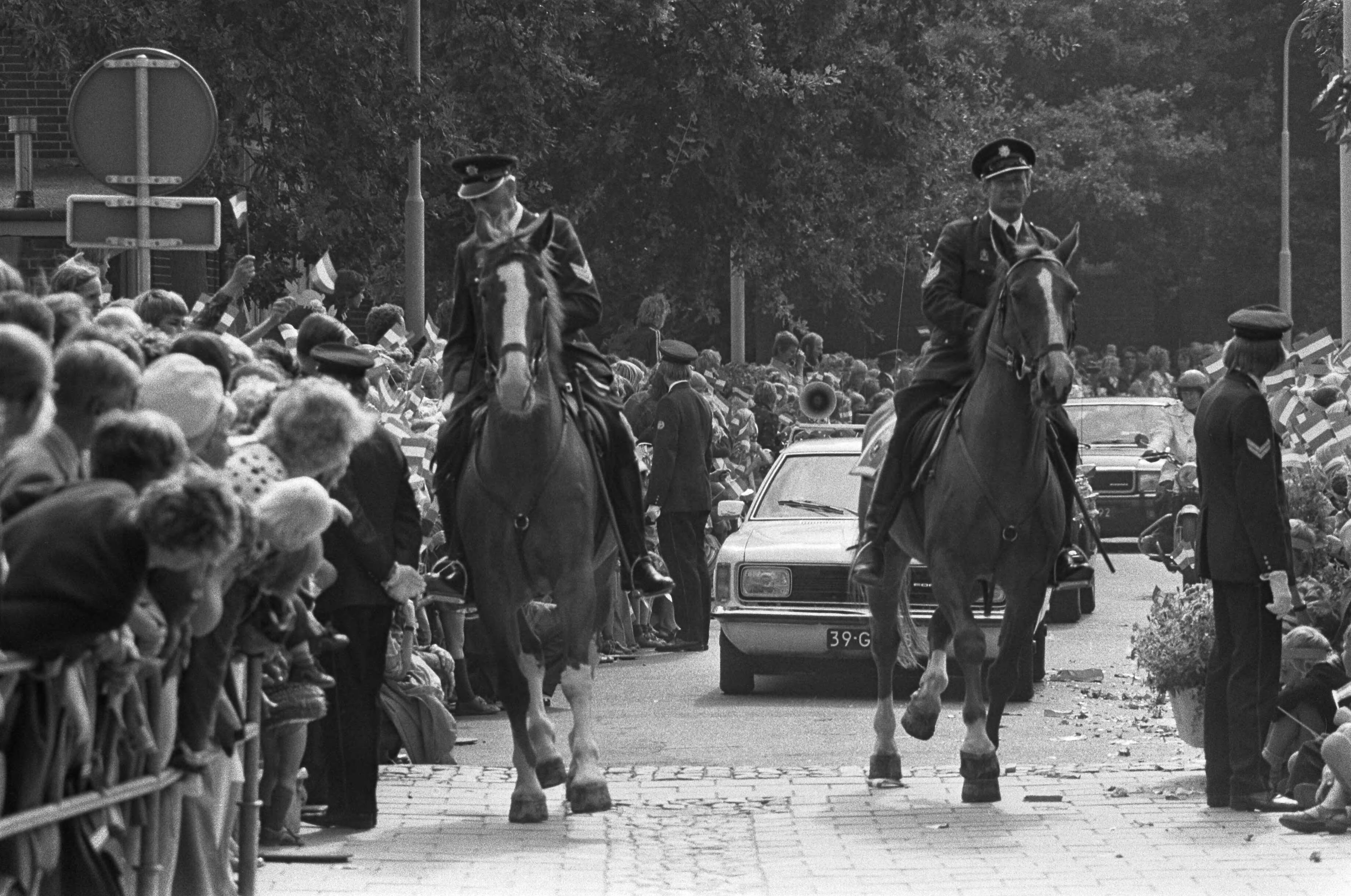 Fotocollectie Anefo — Koningin Juliana bezoekt Haren (Groningen) met bommelding; Koningin passeert de route in een zwaarbewaakte auto, voorafgegaan door politie met paard — Foto: Mieremet, Rob / Anefo. Licentie: Set B: Rechtenvrij / Publiek Domein. Bron: Nationaal Archief. http://hdl.handle.net/10648/ac71a64c-d0b4-102d-bcf8-003048976d84