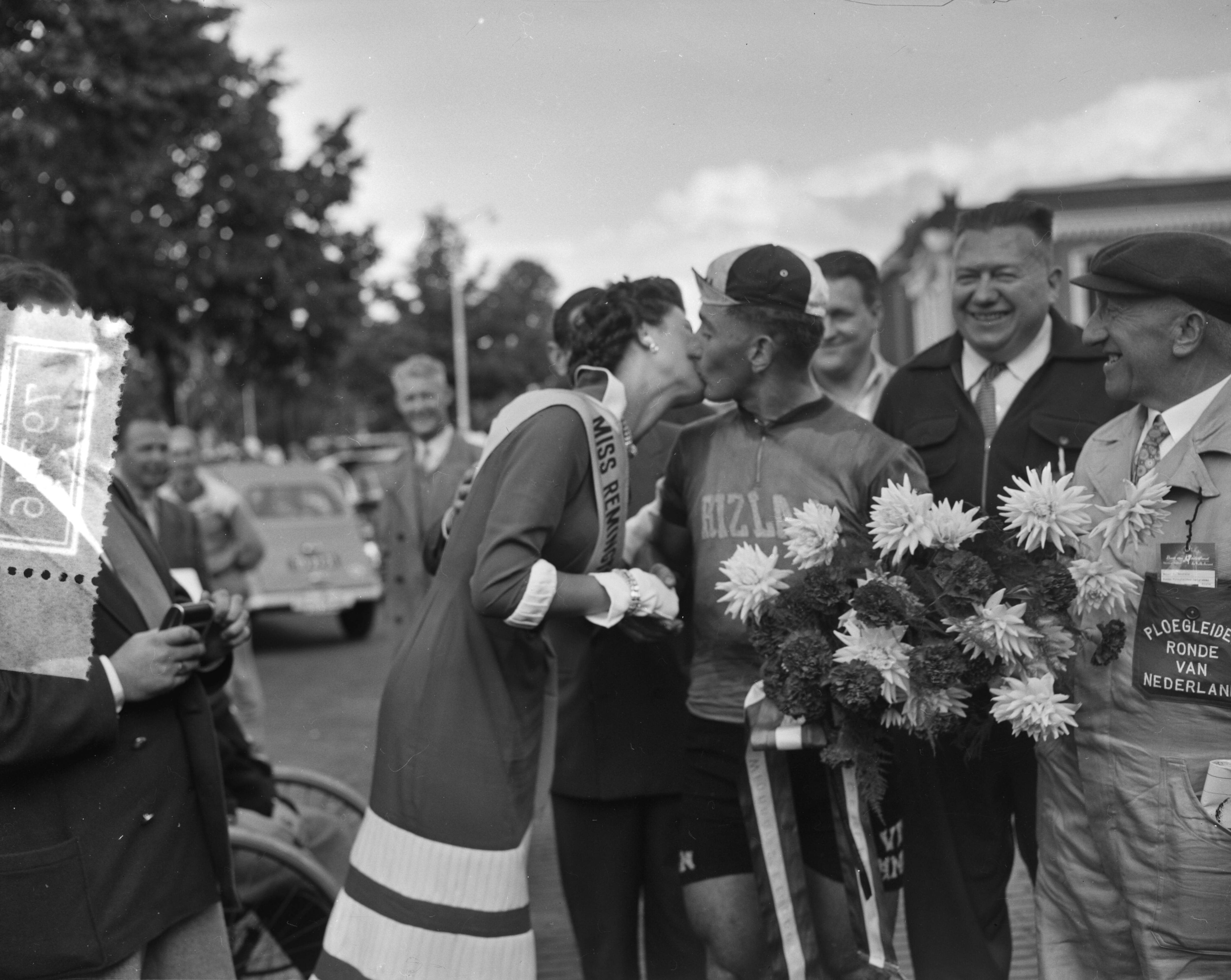 Fotocollectie Anefo — Ronde van Nederland. 2e etappe Steenwijkerwold-Leeuwarden. Etappewinnaar de Belg Willy Vannitsen krijgt kus van Miss Remington. Rechts zijn ploegleider — Foto: Bilsen, Joop van / Anefo. Licentie: Set B: Rechtenvrij / Publiek Domein. Bron: Nationaal Archief. http://hdl.handle.net/10648/a94cfaca-d0b4-102d-bcf8-003048976d84