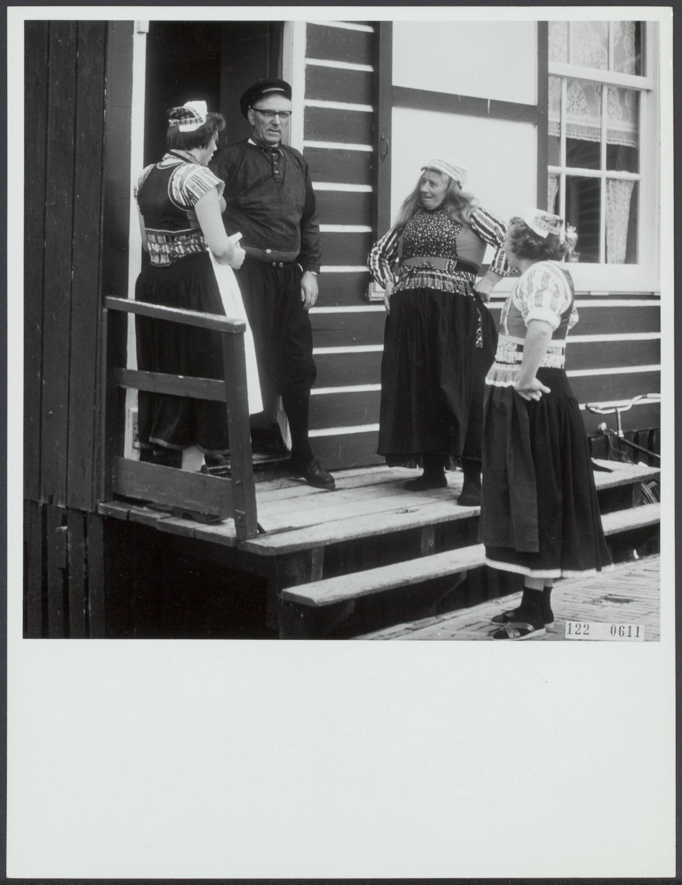 Klederdrachten — [Drie vrouwen in klederdracht en een man praten voor de ingang van een huis] — Foto: Rijksvoorlichtingsdienst (RVD). Licentie: Set B: Rechtenvrij / Publiek Domein. Bron: Nationaal Archief. http://hdl.handle.net/10648/af2b2e3a-d0b4-102d-bcf8-003048976d84