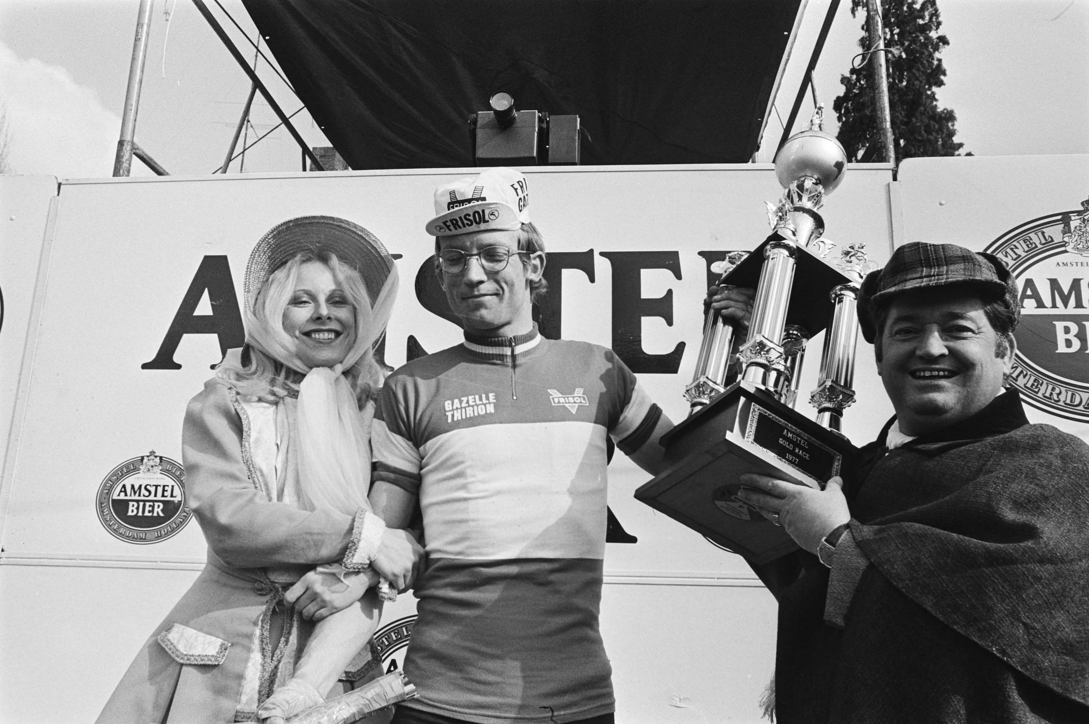 Amstel Gold Race 1977 — Winnaar Jan Raas tijdens de huldiging, geflankeerd door de artiesten Willy Alberti en Bonnie St. Claire. — Foto: Verhoeff, Bert / Anefo. Licentie: Set B: Rechtenvrij / Publiek Domein. Bron: Nationaal Archief. http://hdl.handle.net/10648/ac9969ca-d0b4-102d-bcf8-003048976d84