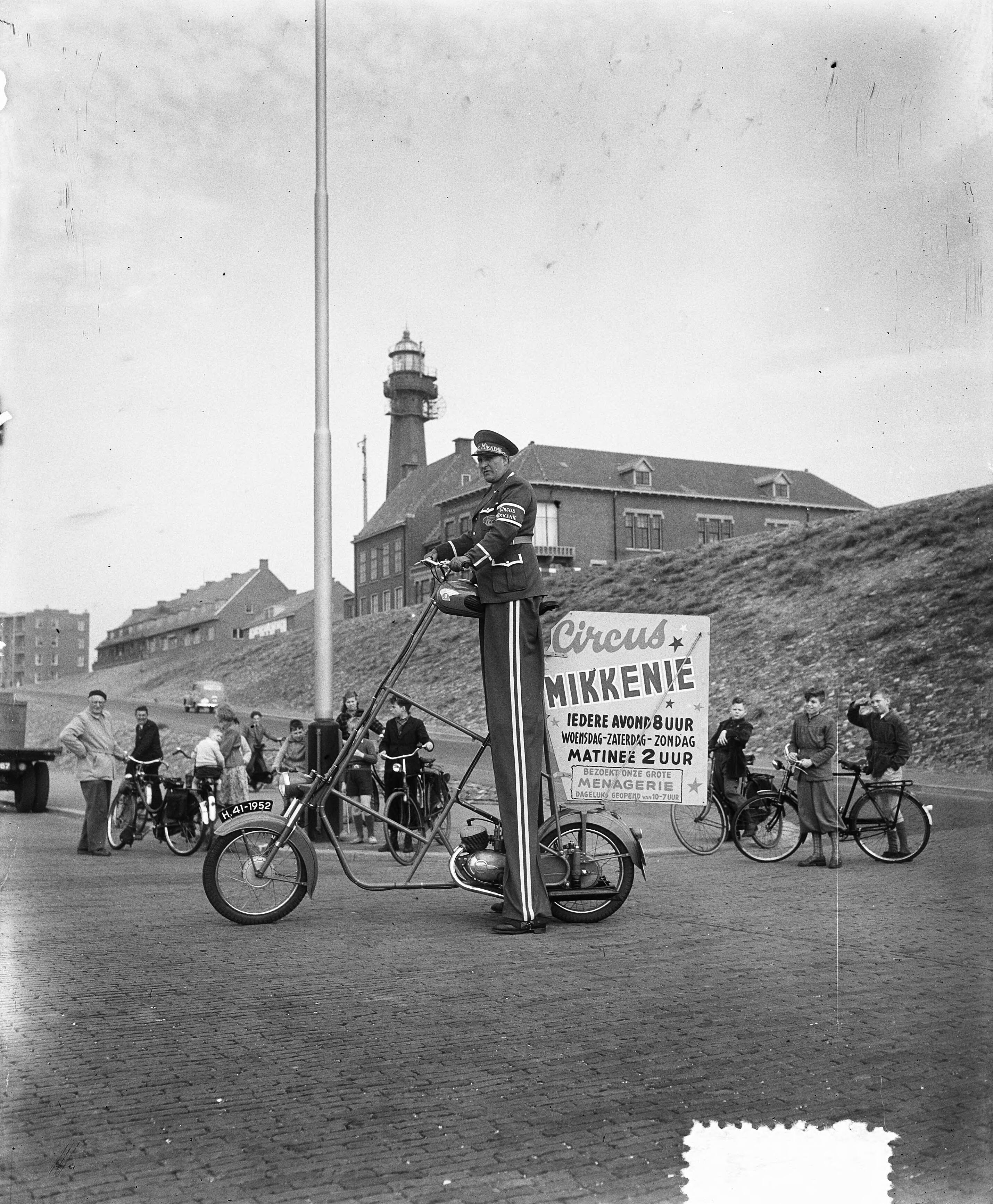 Fotocollectie Anefo — "Reclamereus" van circus Mikkenie (man in uniform op stelten en bijzondere bromfiets) te Scheveningen — Foto: Duinen, H. van / Anefo. Licentie: Set B: Rechtenvrij / Publiek Domein. Bron: Nationaal Archief. http://hdl.handle.net/10648/a8f7d144-d0b4-102d-bcf8-003048976d84