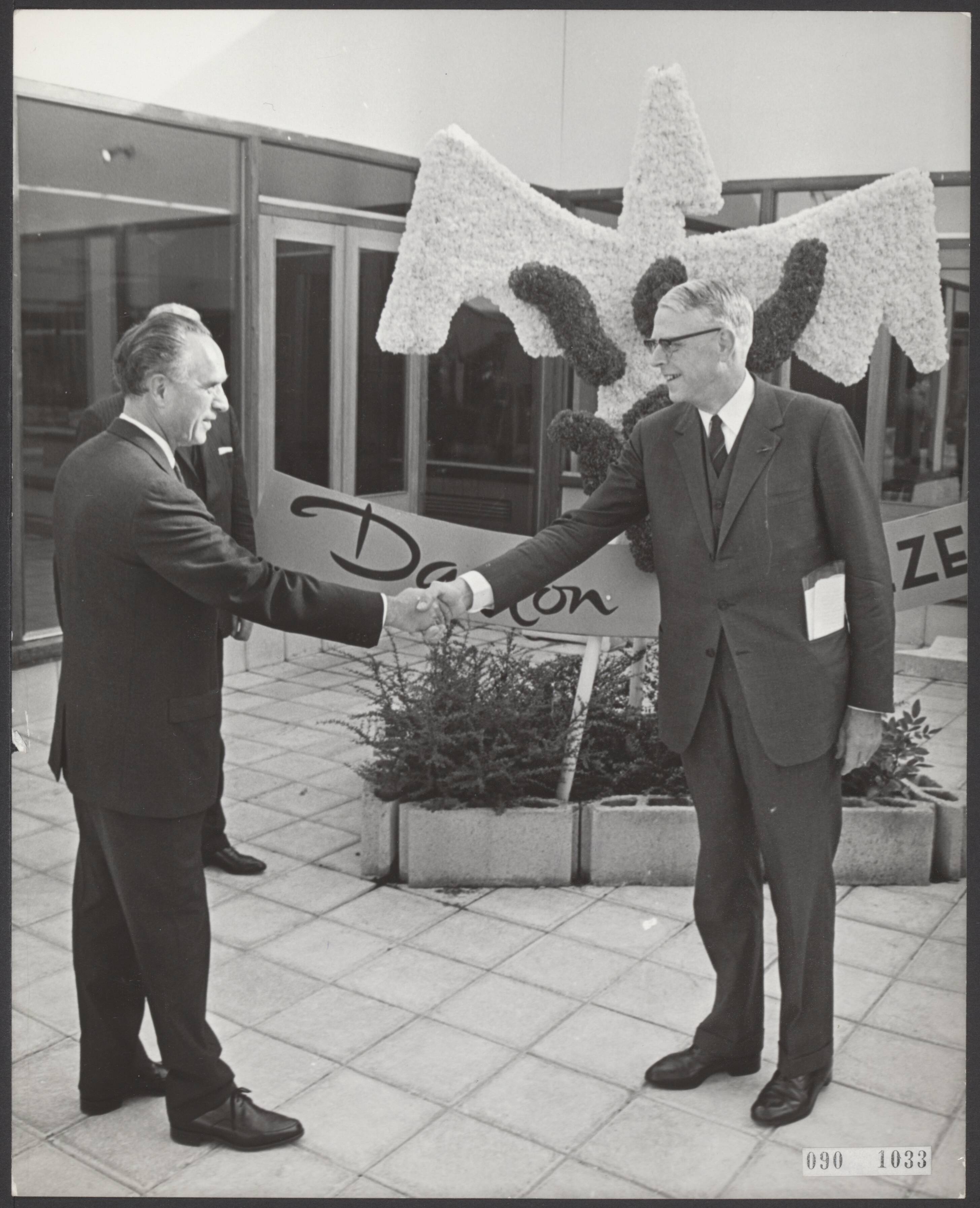 Fotocollectie Elsevier Binnenland — Minister mr. L. de Block heeft de uit de as herrezen Danlon kousenfabriek officiëel geopend te Emmen. Na de openingswoorden drukte hij op een knop waardoor een uit bloemen gemaakte Phoenix werd onthuld. Hij feliciteert H.C. Andersen, president-directeur van de Danlon fabrieken (links) — Foto: Nijs, Jac. de / Anefo. Licentie: Set B: Rechtenvrij / Publiek Domein. Bron: Nationaal Archief. http://hdl.handle.net/10648/ae1daa18-d0b4-102d-bcf8-003048976d84