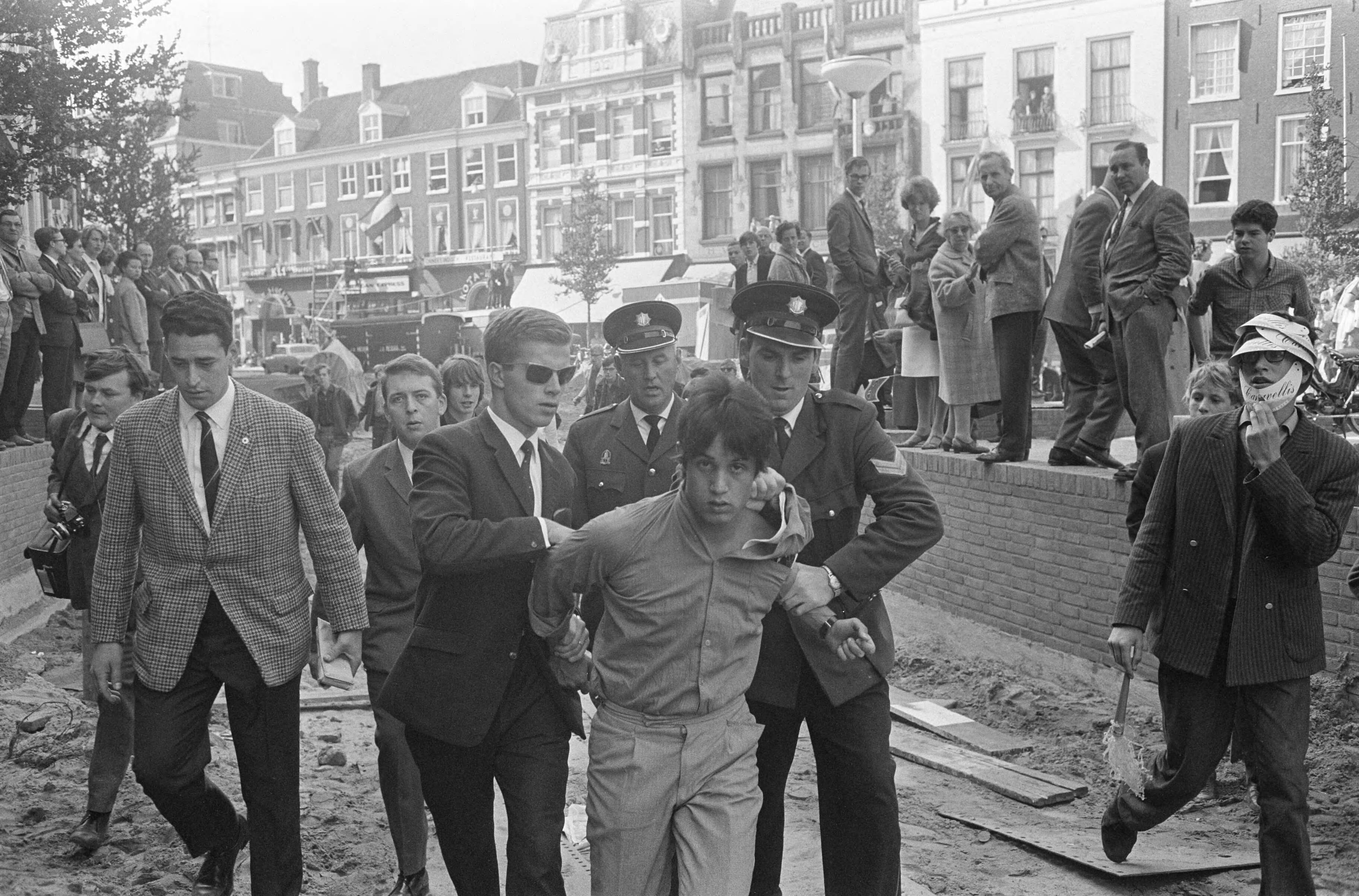 Protesterende Amsterdamse Provo's tijdens Prinsjesdag 1966 in Den Haag — Arrestatie van een lid van de Amsterdamse Provo — Foto: Fotograaf Onbekend / Anefo. Licentie: Set B: Rechtenvrij / Publiek Domein. Bron: Nationaal Archief. http://hdl.handle.net/10648/aafd4a6e-d0b4-102d-bcf8-003048976d84