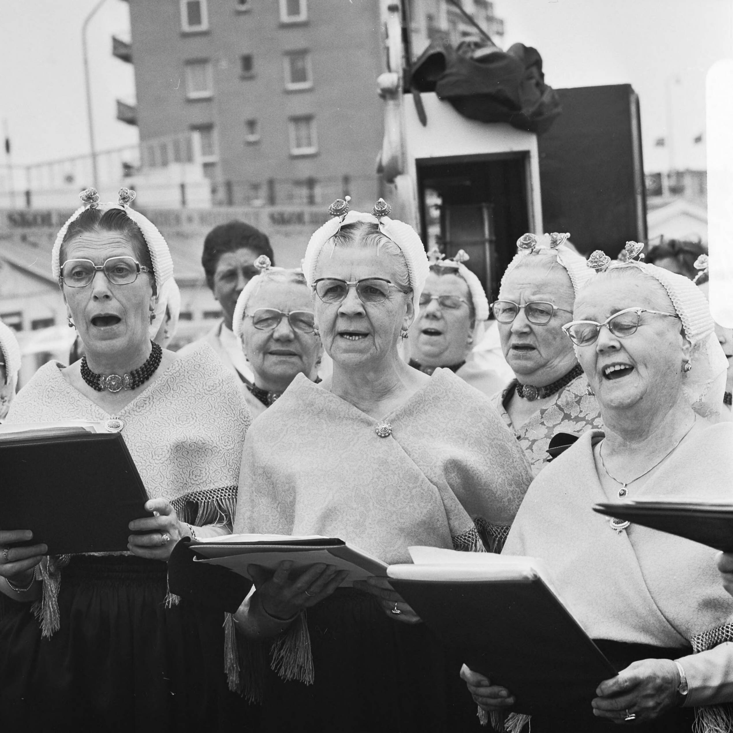 Fotocollectie Anefo — VVV-directeuren brengen zak zand naar jubilerende VVV in Scheveningen; zingende Scheveningse vrouwen in klederdracht — Foto: Mieremet, Rob / Anefo. Licentie: Set B: Rechtenvrij / Publiek Domein. Bron: Nationaal Archief. http://hdl.handle.net/10648/ac4ae1c4-d0b4-102d-bcf8-003048976d84
