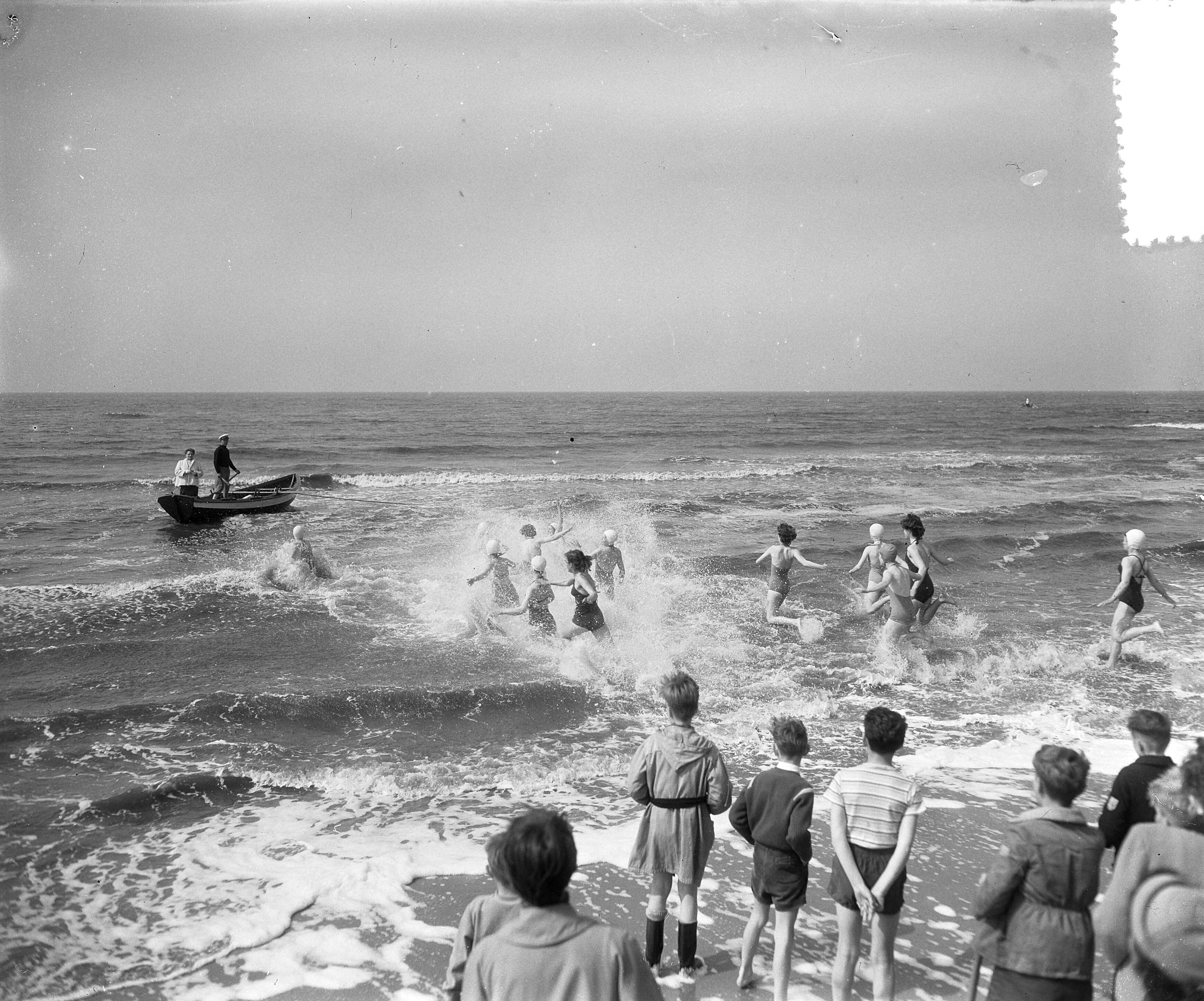 Fotocollectie Anefo — "Wedloop naar zee" te Scheveningen [een groep vrouwen in badkleding rennen de zee in, naar een roeiboot in de branding, waar een vrouw klaarstaat met een voorwerp] — Foto: Rossem, Wim van / Anefo. Licentie: Set B: Rechtenvrij / Publiek Domein. Bron: Nationaal Archief. http://hdl.handle.net/10648/a935f67c-d0b4-102d-bcf8-003048976d84