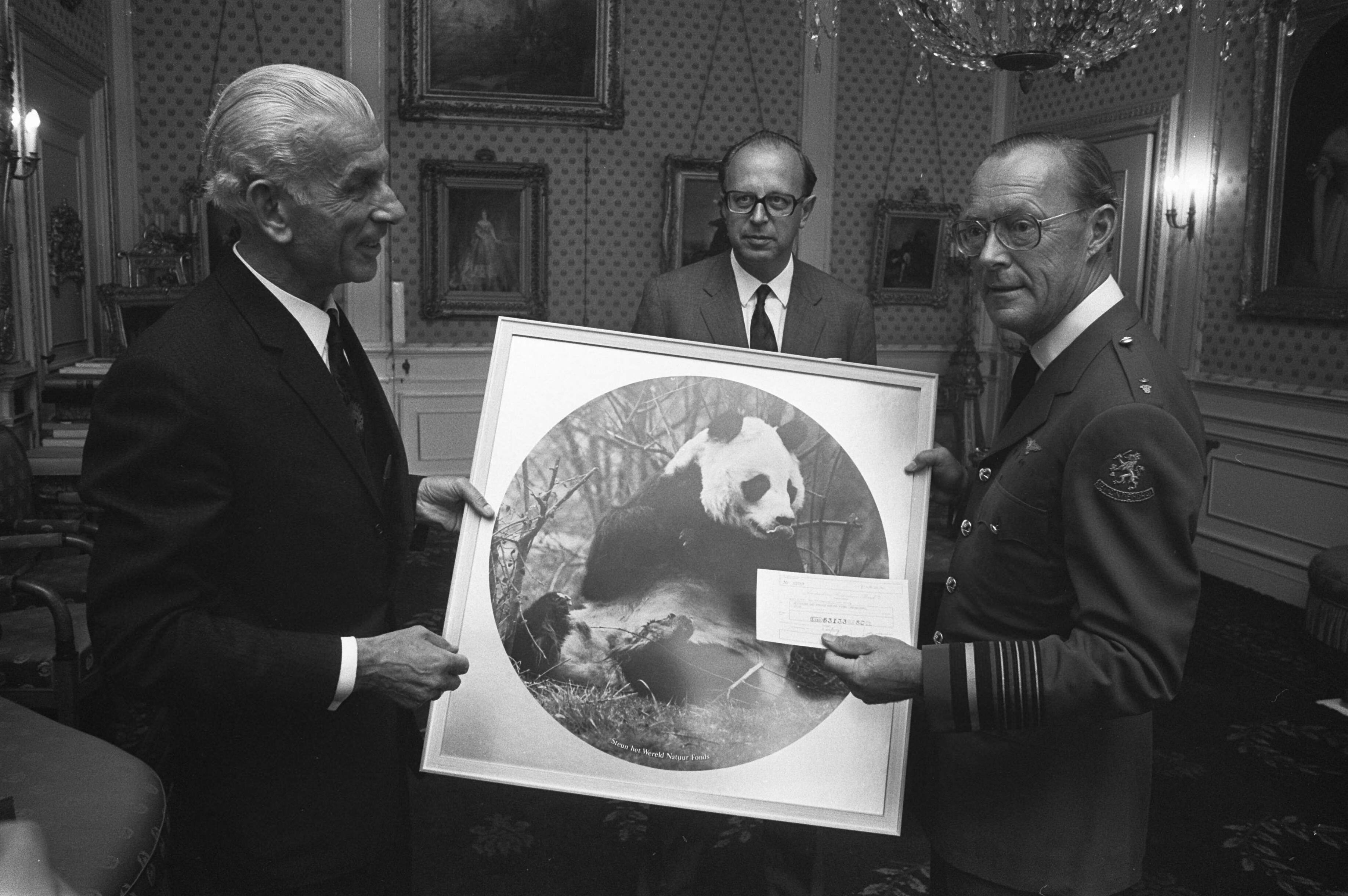 Ontvangst op Soestdijk door Prins Bernhard van een delegatie van Esso, in verband met een actie voor het Wereld Natuur Fonds — De delegatie overhandigt de prins een ingelijste foto van een pandabeer, het symbool van het Wereld Natuur Fonds, en een envelop — Foto: Fotograaf Onbekend / Anefo. Licentie: Set B: Rechtenvrij / Publiek Domein. Bron: Nationaal Archief. http://hdl.handle.net/10648/abe92a88-d0b4-102d-bcf8-003048976d84