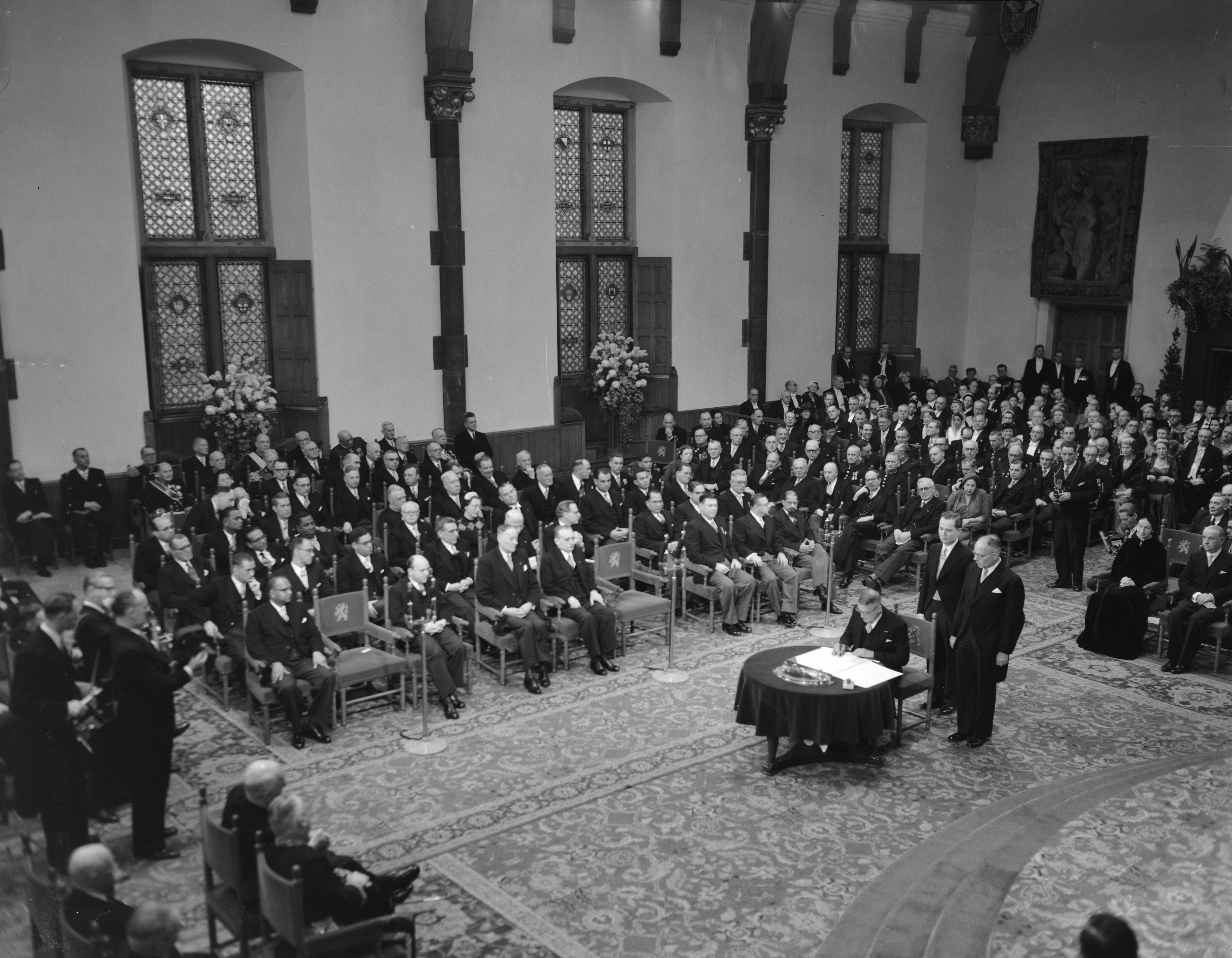 Koningin Juliana ondertekent in een plechtige bijeenkomst in de Ridderzaal in Den Haag de Acte van Bevestiging van het Statuut voor het Koninkrijk — Ondertekening van de Acte van Bevestiging van het Statuut van het Koninkrijk in de Ridderzaal te Den Haag. Verschillende ministers ondertekenen de akte — Foto: Noske, J.D. / Anefo. Licentie: Set B: Rechtenvrij / Publiek Domein. Bron: Nationaal Archief. http://hdl.handle.net/10648/a92e2046-d0b4-102d-bcf8-003048976d84