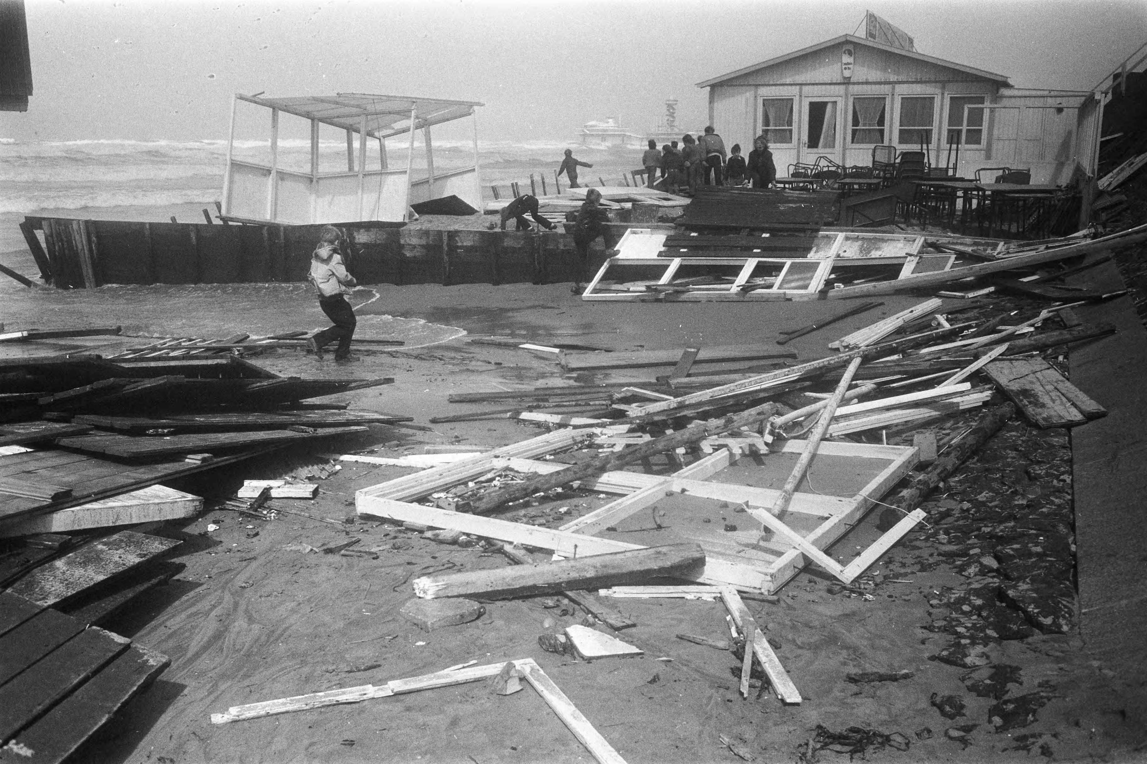 Stormschade aan strandtenten te Scheveningen — Brokstukken en onderdelen van de starndtenten verspreid over het strand — Foto: Fotograaf Onbekend / Anefo. Licentie: Set B: Rechtenvrij / Publiek Domein. Bron: Nationaal Archief. http://hdl.handle.net/10648/ab958bbc-d0b4-102d-bcf8-003048976d84