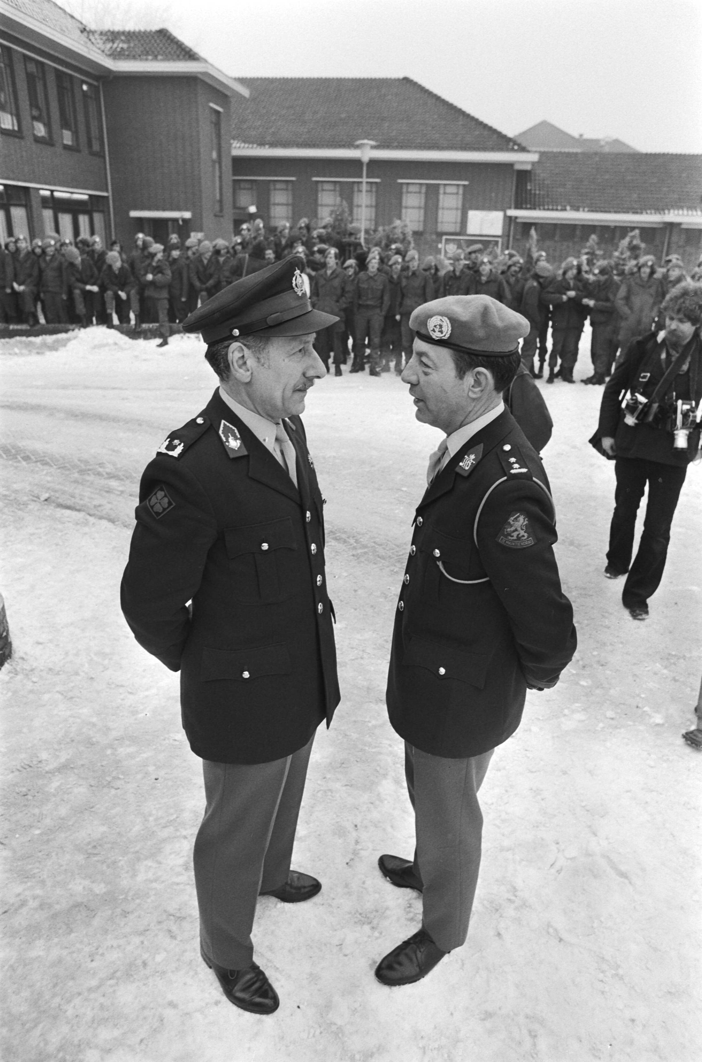 Prinses Beatrix en prins Claus bezoeken VN detachement voor Libanon in de Adolf van Nassau kazerne in Zuidlaren — Onderonsje tussen twee officieren op een besneeuwd terrein — Foto: Suyk, Koen / Anefo. Licentie: Set B: Rechtenvrij / Publiek Domein. Bron: Nationaal Archief. http://hdl.handle.net/10648/acc4c9bc-d0b4-102d-bcf8-003048976d84