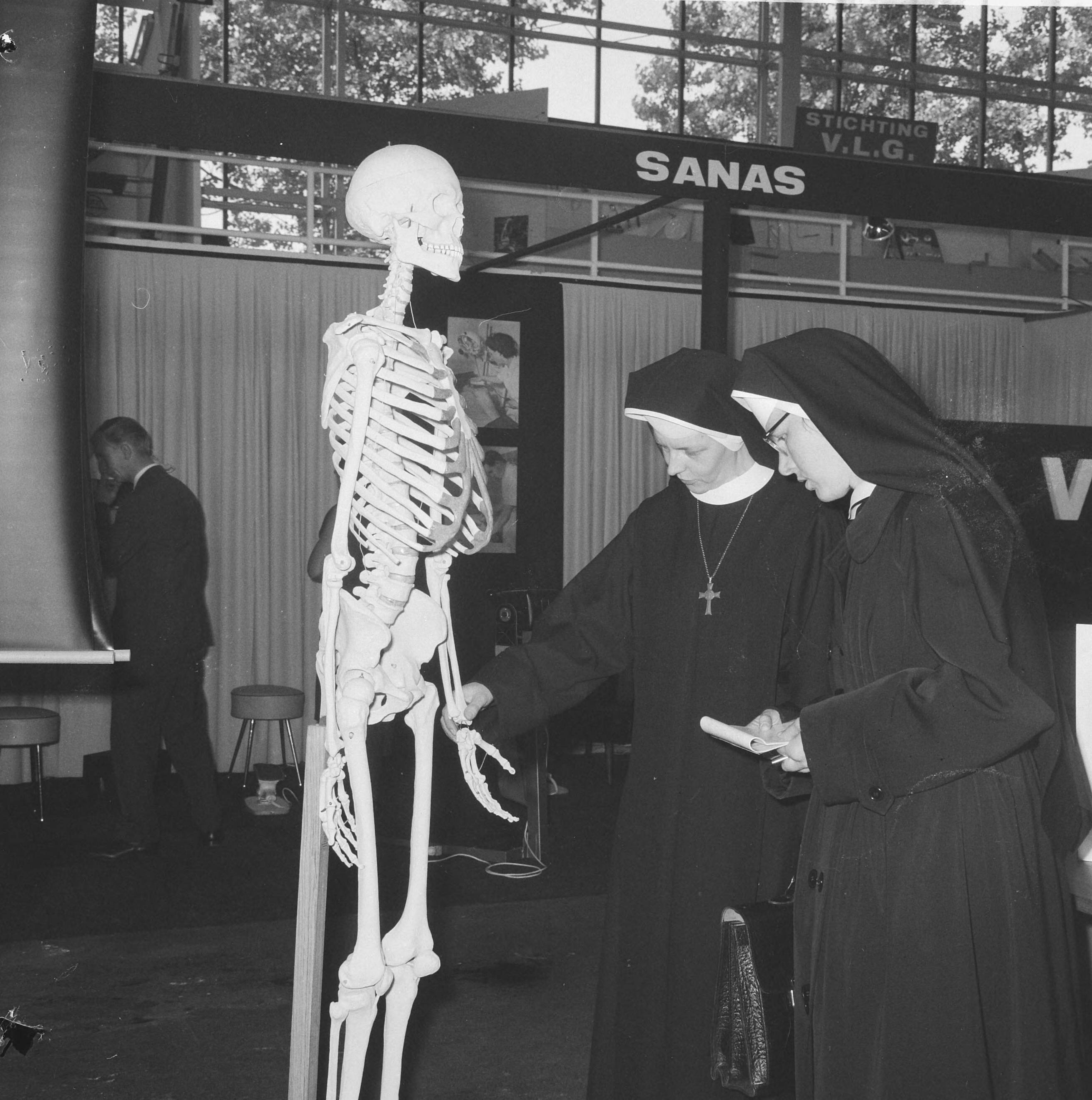 Fotocollectie Anefo — Vakbeurs Medica 65 in Expohal te Hilversum, verpleegsters (nonnen) bij geraamte — Foto: Nijs, Jac. de / Anefo. Licentie: Set B: Rechtenvrij / Publiek Domein. Bron: Nationaal Archief. http://hdl.handle.net/10648/aac1f572-d0b4-102d-bcf8-003048976d84