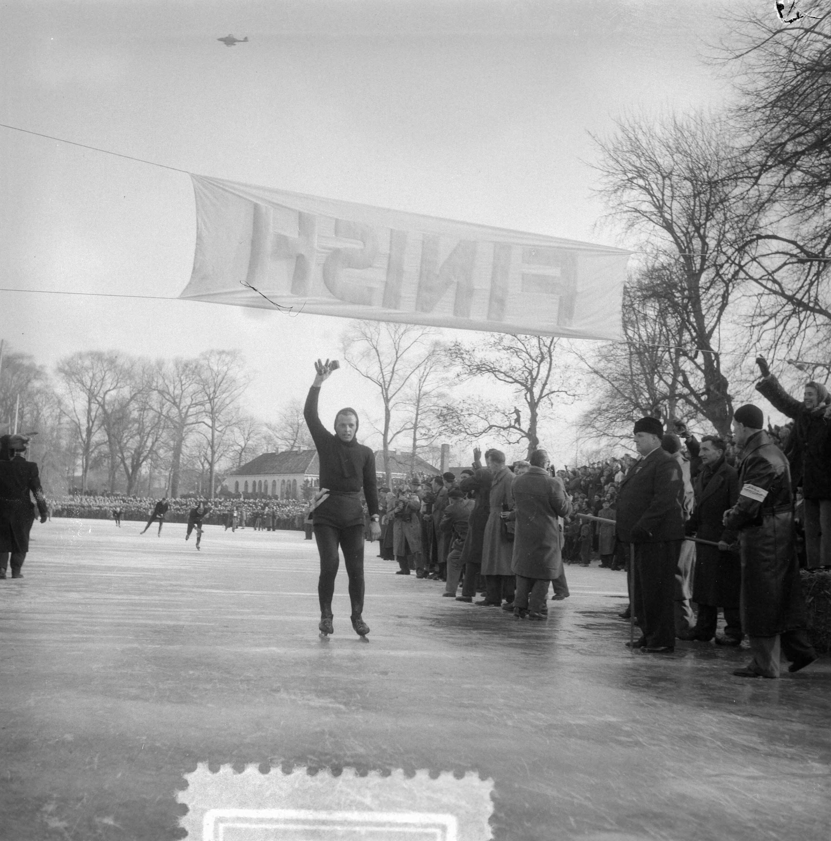 Elfstedentocht 1954 — Elfstedentocht. Jeen van den Berg passeert de finish — Foto: Noske, J.D. / Anefo. Licentie: Set B: Rechtenvrij / Publiek Domein. Bron: Nationaal Archief. http://hdl.handle.net/10648/a91c5762-d0b4-102d-bcf8-003048976d84