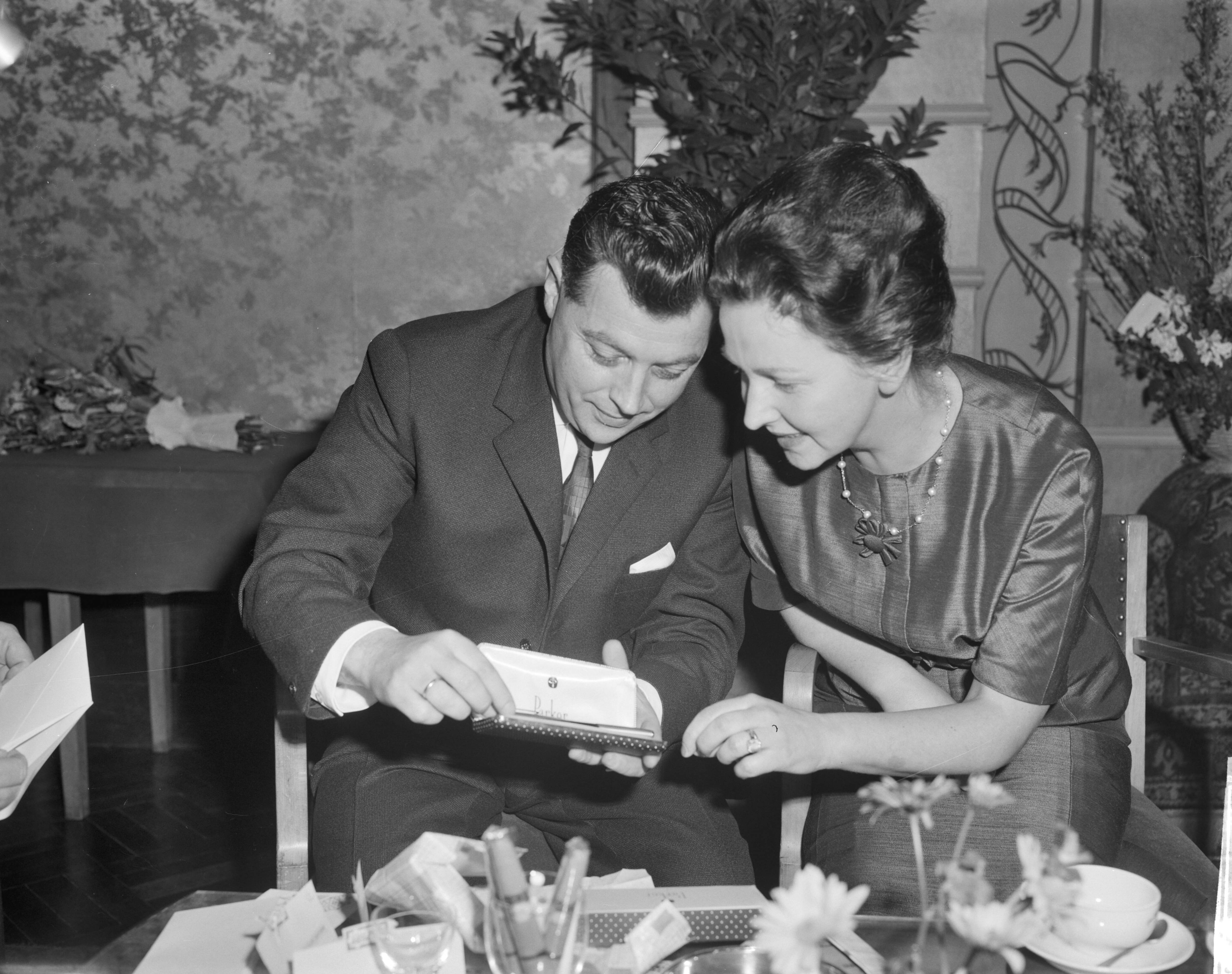 Fotocollectie Anefo — Carel Enkelaar heeft afscheid genomen als hoofd van het NTS-journaal in Hof van Holland te Hilversum, Carel Enkelaar en zijn vrouw bekijken geschenken (een pennenset) — Foto: Bilsen, Joop van / Anefo. Licentie: Set B: Rechtenvrij / Publiek Domein. Bron: Nationaal Archief. http://hdl.handle.net/10648/aa2843d2-d0b4-102d-bcf8-003048976d84