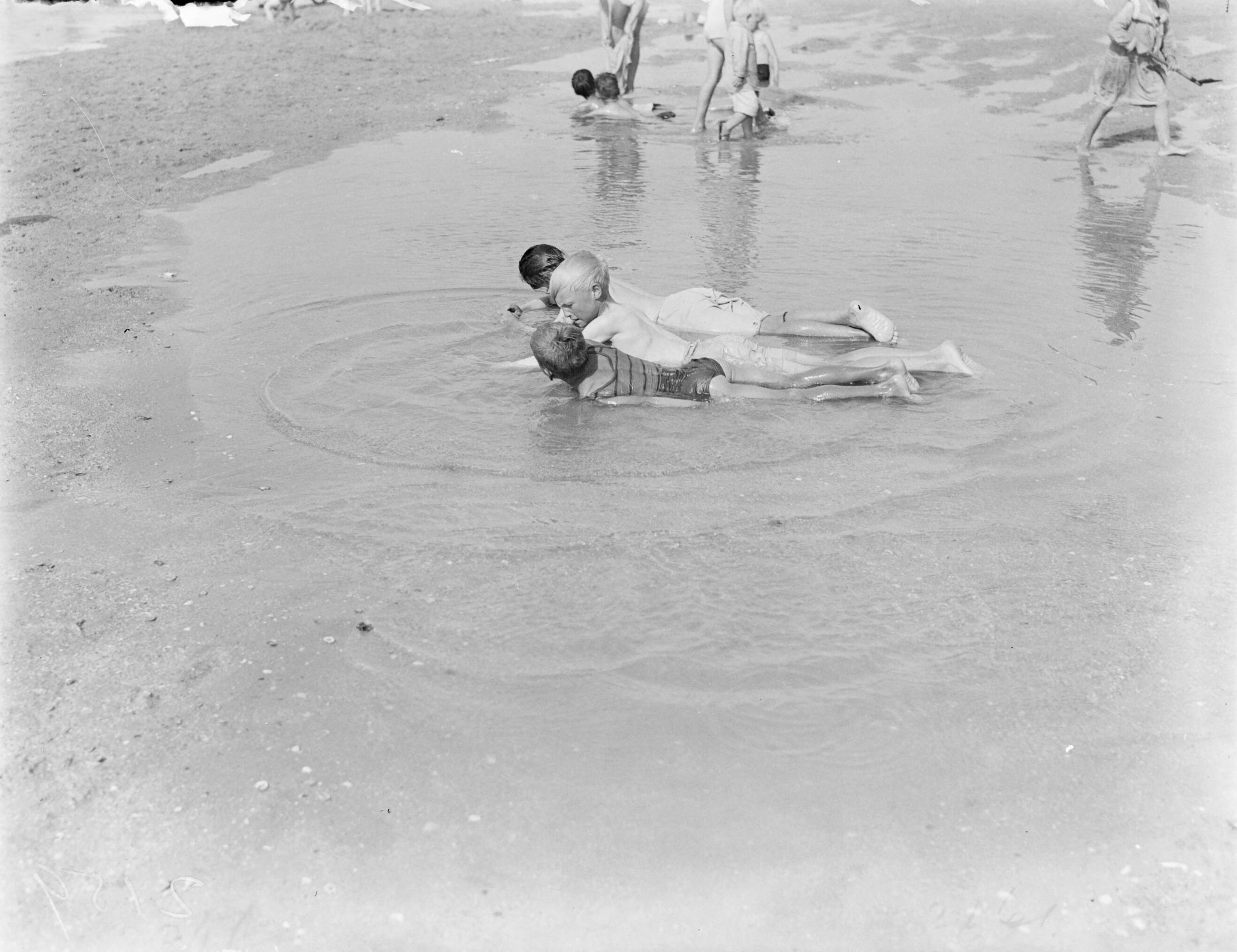 Strandtaferelen Scheveningen — Kinderen liggend in ondiep water — Foto: Poll, Willem van de. Licentie: Set B: Rechtenvrij / Publiek Domein. Bron: Nationaal Archief. http://hdl.handle.net/10648/aea865fe-d0b4-102d-bcf8-003048976d84