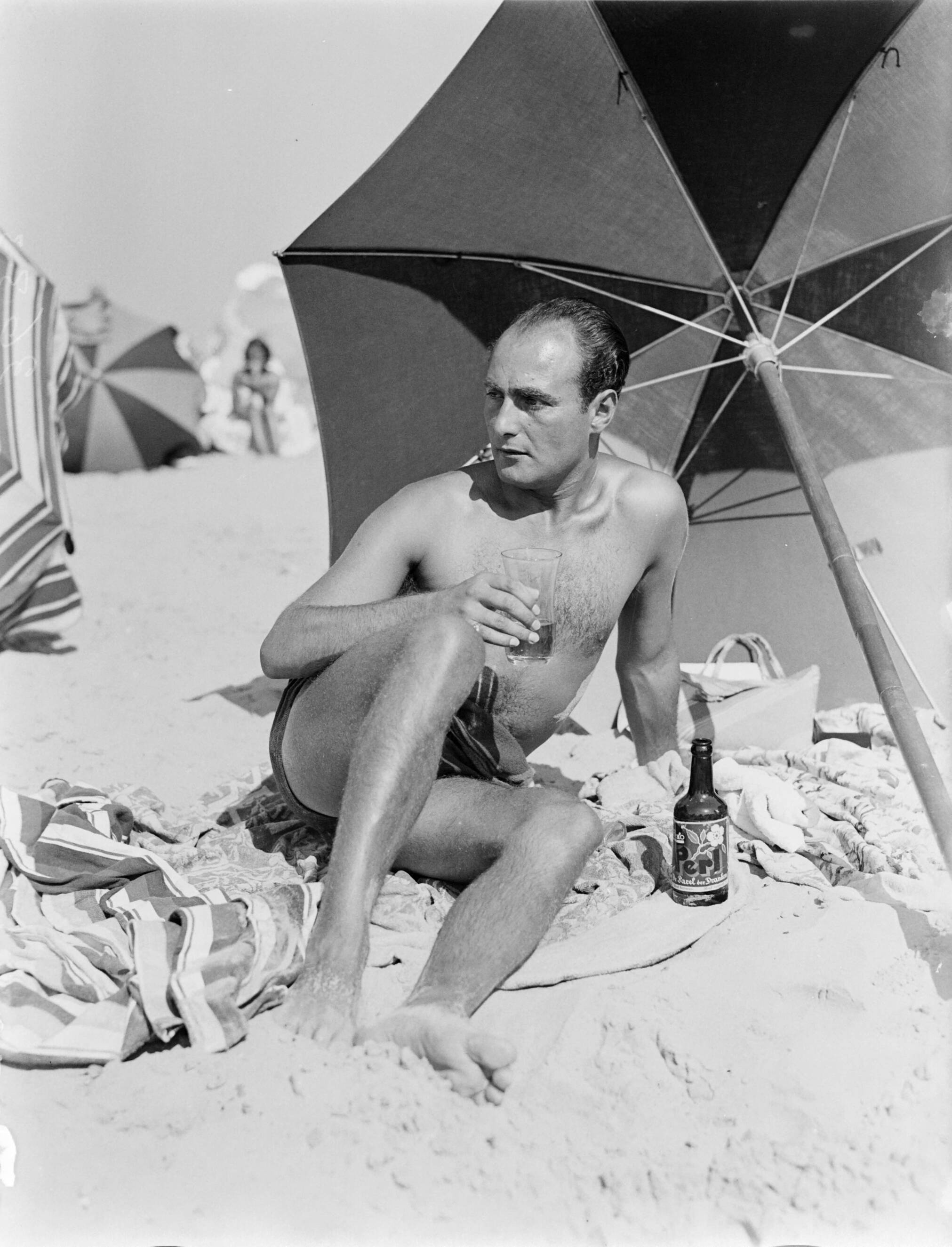 Scheveningen. — Een man [Farrar] op het Scheveningse strand onder een parasol — Foto: Poll, Willem van de. Licentie: Set B: Rechtenvrij / Publiek Domein. Bron: Nationaal Archief. http://hdl.handle.net/10648/aea00148-d0b4-102d-bcf8-003048976d84