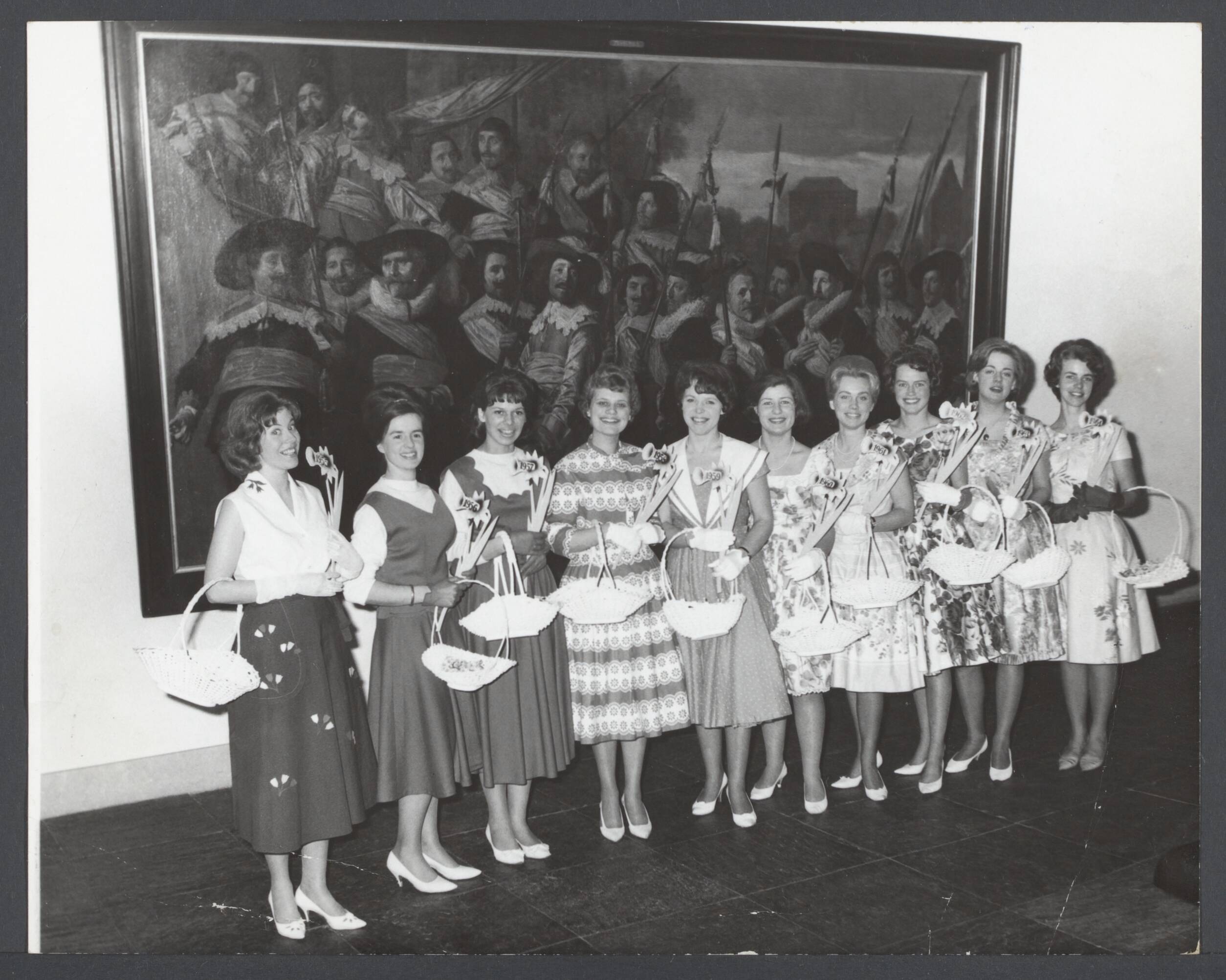 Bloemenmeisjes III — Door de Haarlemse gemeenteraad en de directie van Haarlems Bloei werd in het Frans Halsmuseum een receptie gegeven t.g.v. het 10-jarig bestaan van de Haarlemse Bloemenmeisjes en de opening van het Bollenseizoen. De bloemenmeisjes waren vertegenwoordigd door tien verschillende kostuums, nl. van 1955 t/m 1964. Zij poseren voor het meesterwerk van Frans Hals "officieren en onderofficieren" — Foto: Pot, Harry / Anefo. Licentie: Set B: Rechtenvrij / Publiek Domein. Bron: Nationaal Archief. http://hdl.handle.net/10648/503c3f50-3101-14b9-3d32-5dd61db3a418