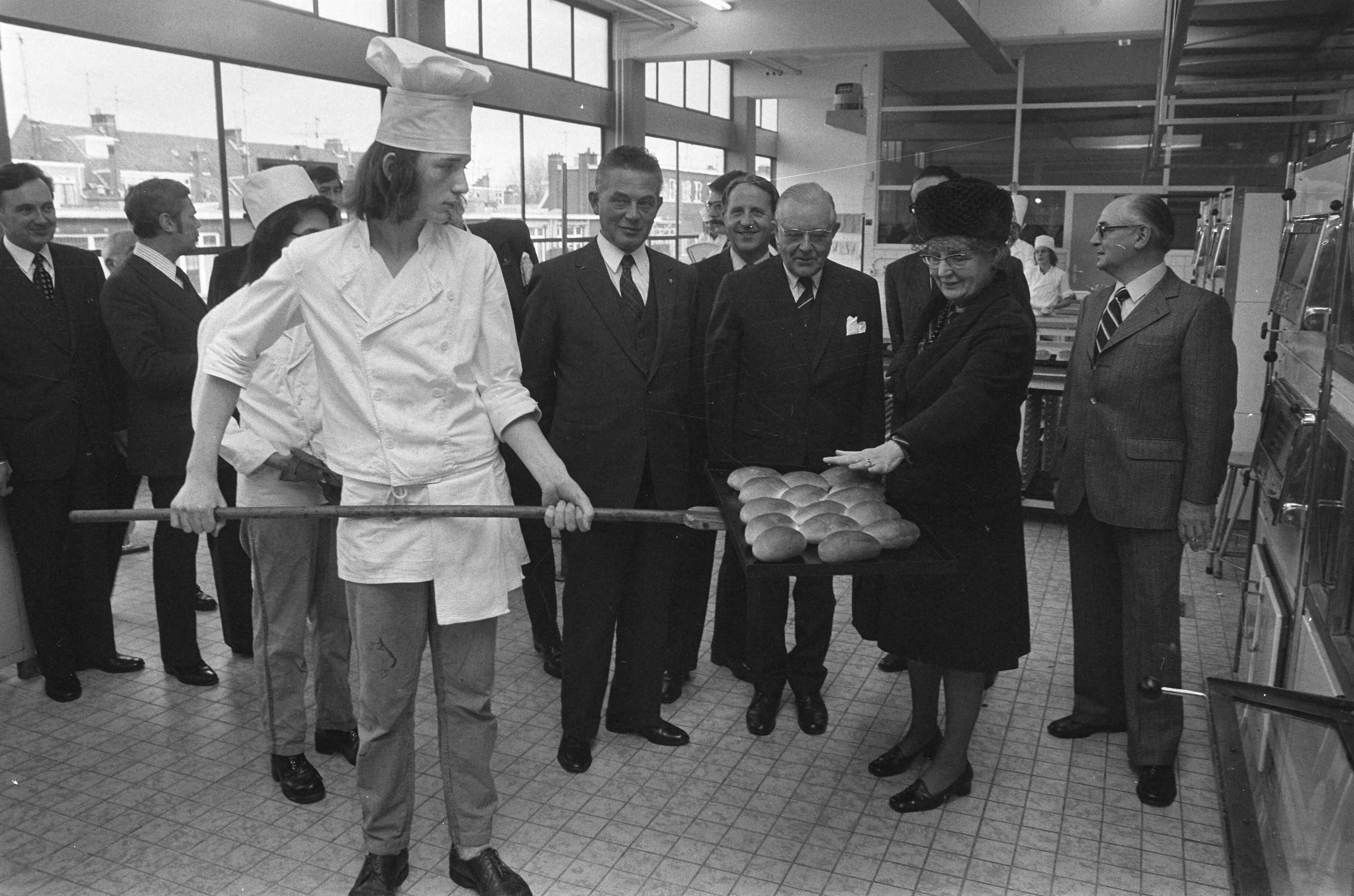 Koningin Juliana bezoekt scholen in Den Haag — De koningin voelt de warmte van broodjes uit de oven in de Vatelschool — Foto: Fotograaf Onbekend / Anefo. Licentie: Set B: Rechtenvrij / Publiek Domein. Bron: Nationaal Archief. http://hdl.handle.net/10648/ac3c3908-d0b4-102d-bcf8-003048976d84