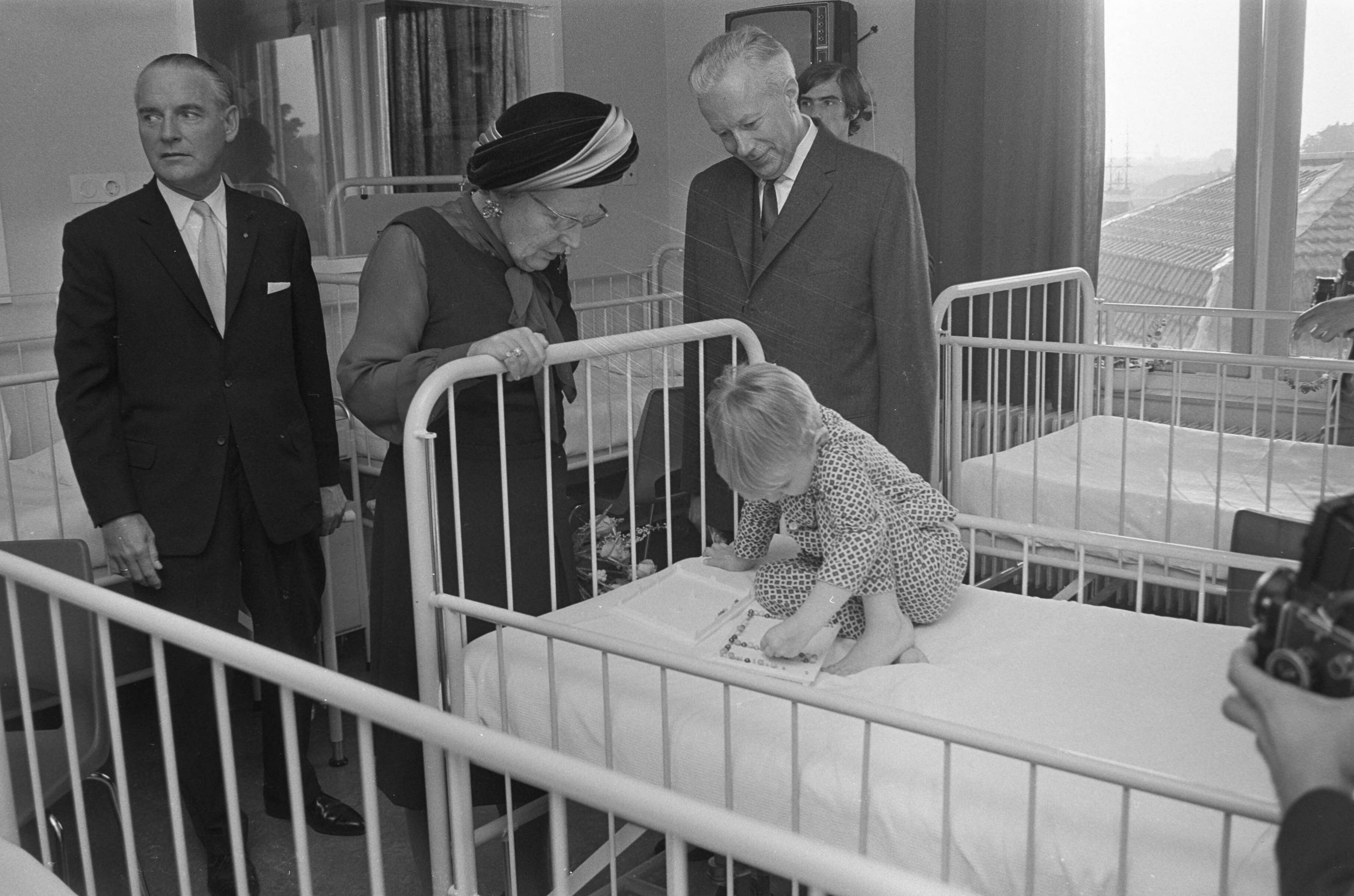 Hare Majesteit koningin Juliana opent het Gasthuis voor Ooglijders in Utrecht — Koningin Juliana bij een patiëntje, naast Hare Majesteit geneeskundig directeur K.W.J.N. Hoppenbrouwers — Foto: Fotograaf Onbekend / Anefo. Licentie: Set B: Rechtenvrij / Publiek Domein. Bron: Nationaal Archief. http://hdl.handle.net/10648/abd23cba-d0b4-102d-bcf8-003048976d84