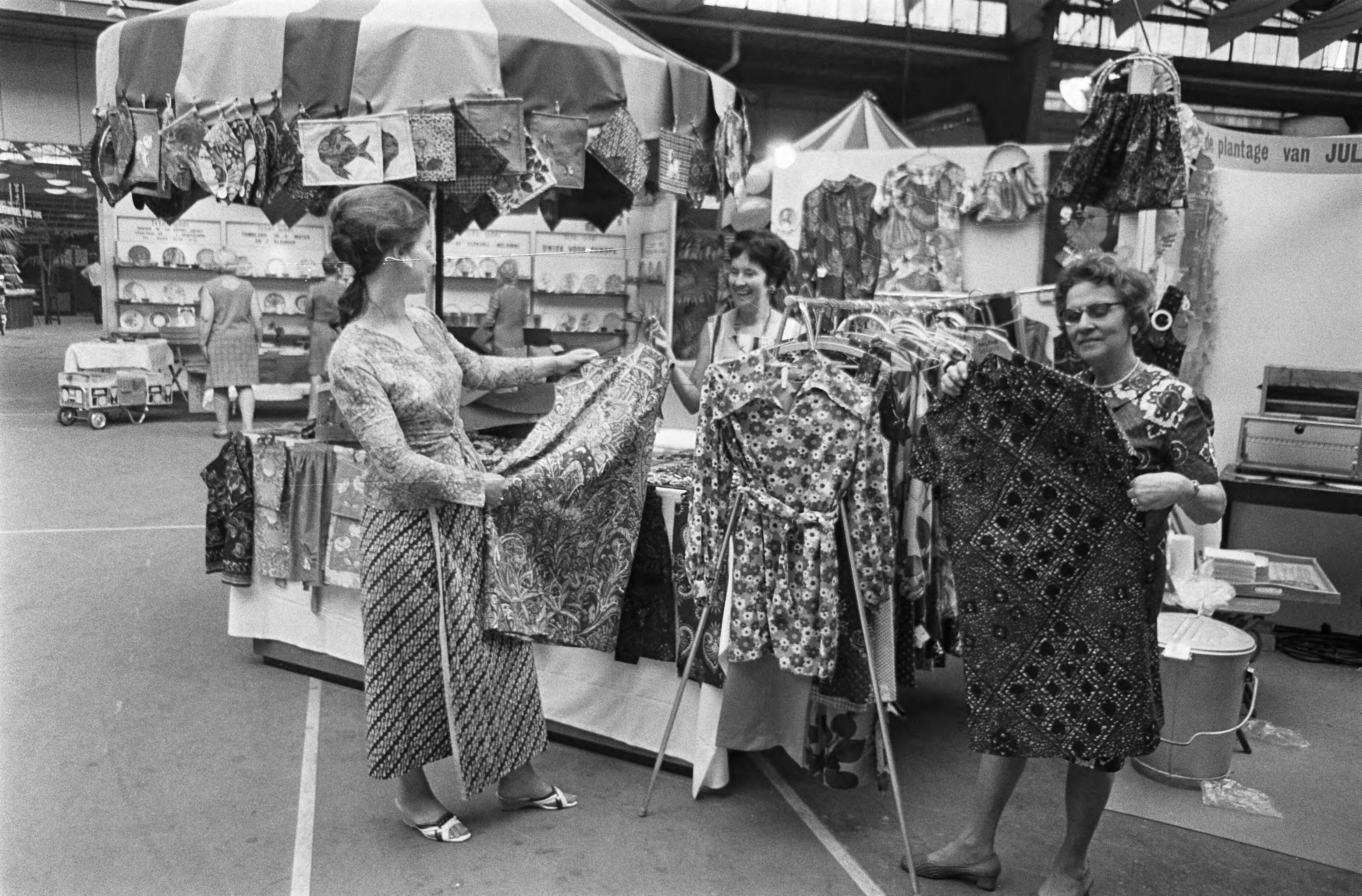 11e Pasar Malam te Den Haag — Een stalletje met sarongs e.d. — Foto: Fotograaf Onbekend / Anefo. Licentie: Set B: Rechtenvrij / Publiek Domein. Bron: Nationaal Archief. http://hdl.handle.net/10648/ab700ae0-d0b4-102d-bcf8-003048976d84