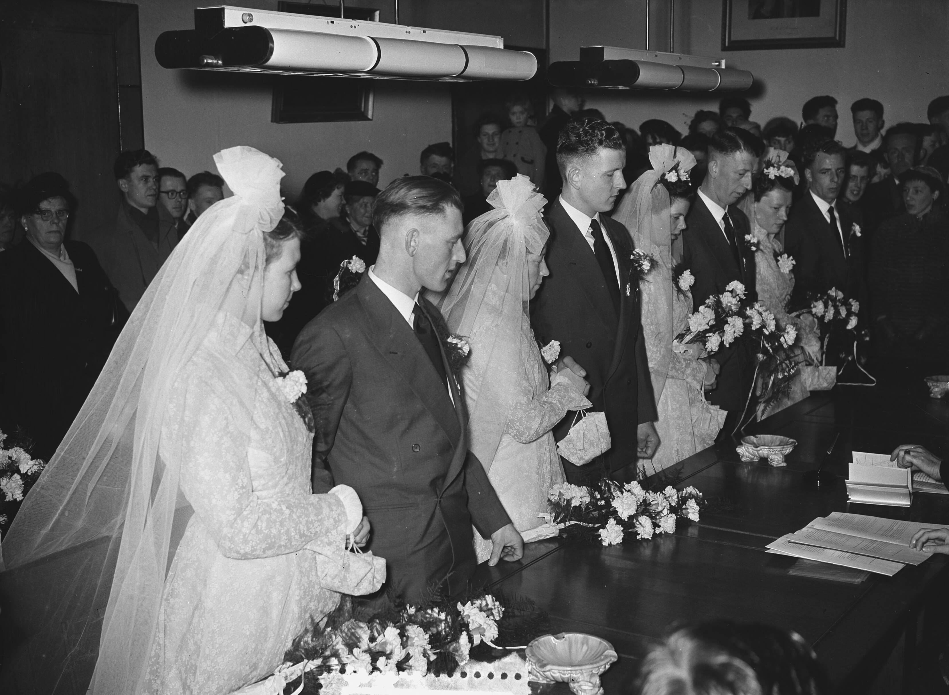 Fotocollectie Anefo — Meervoudige bruiloft. Op het gemeentehuis van Leimuiden trouwden vier telgen uit het gezin Brand (15 kinderen) tegelijkertijd. Vlnr. Het zijn van links naar rechts: Toon Brand (28 jaar, chauffeur) en Catharina Lemmens, Nellie Brand (23 jaar) en Theo Obdam (timmerman), Bram Brand (26 jaar, metselaar) en Bep Könst, en Dora Brand (24 jaar) en Kees Könst (bloemist) — Foto: Pot, Harry / Anefo. Licentie: Set B: Rechtenvrij / Publiek Domein. Bron: Nationaal Archief. http://hdl.handle.net/10648/a930cbe8-d0b4-102d-bcf8-003048976d84