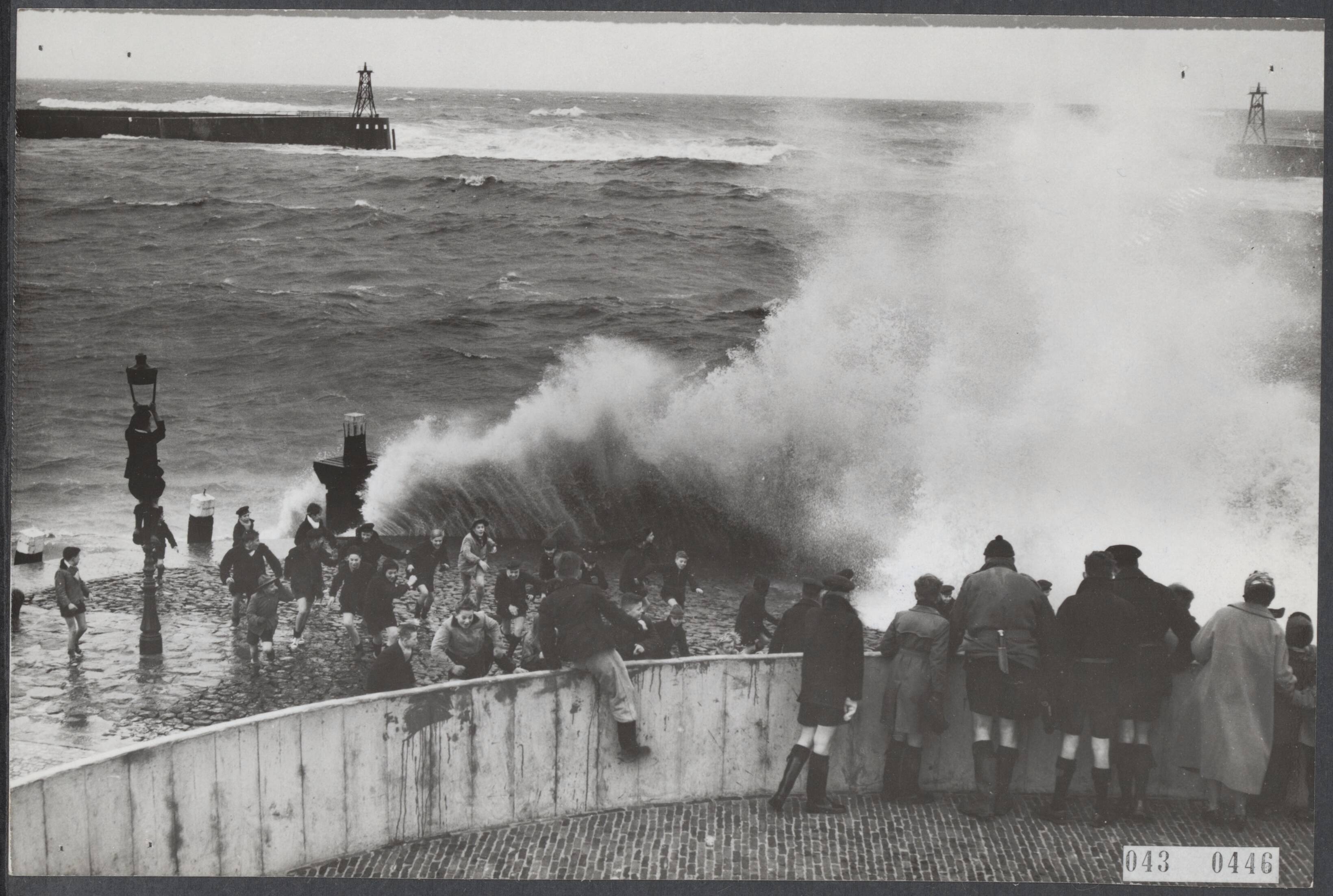Fotocollectie Elsevier Binnenland — Storm langs de Nederlandse kust. Te Scheveningen bij de vissershaven sloeg de zee met donderend geraas over de stenen wal. Voor de kinderen een spel, maar een gevaarlijk spel om voor het water weg te vluchten — Foto: Fotograaf Onbekend / Anefo. Licentie: Set B: Rechtenvrij / Publiek Domein. Bron: Nationaal Archief. http://hdl.handle.net/10648/adf90366-d0b4-102d-bcf8-003048976d84