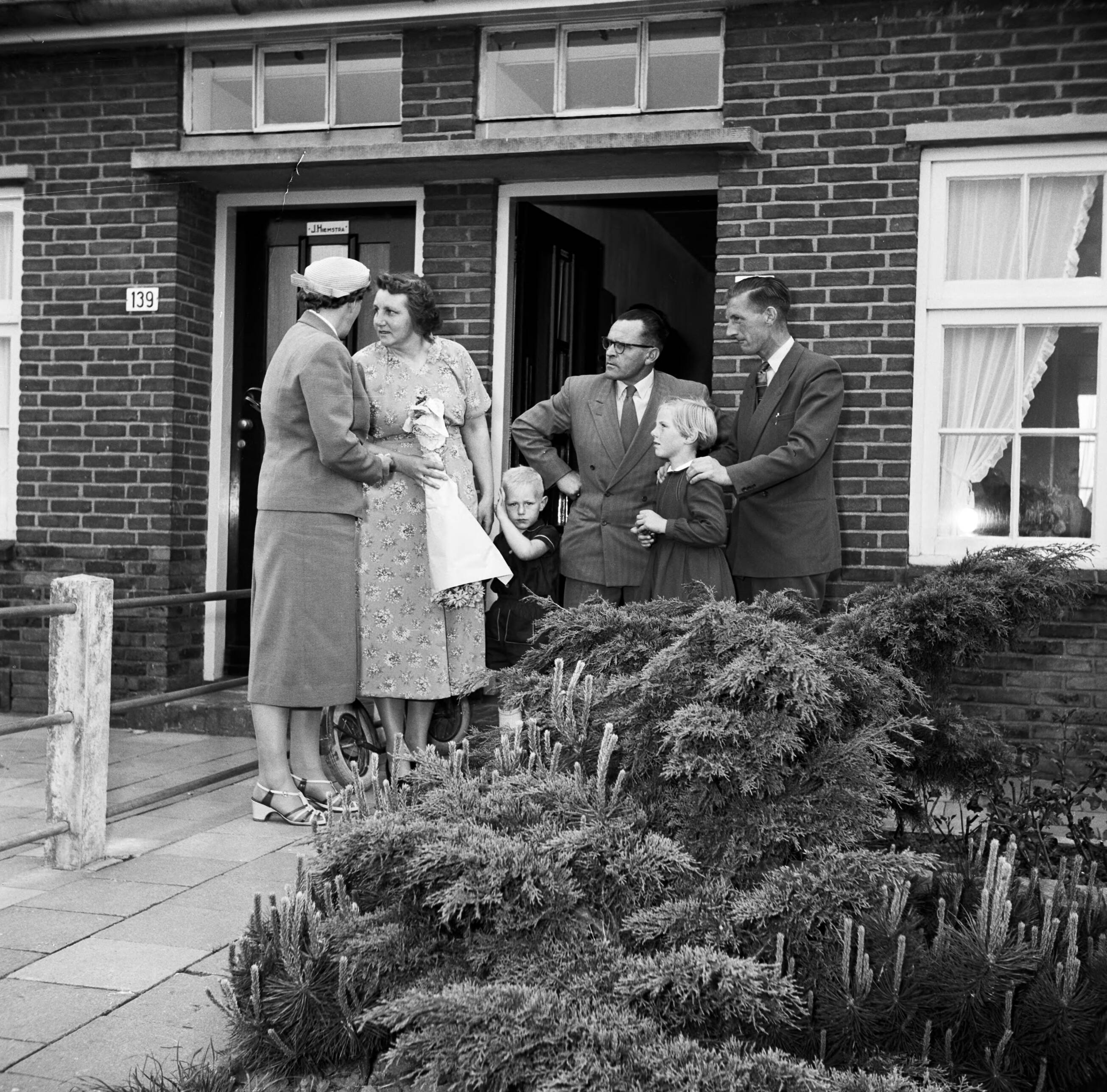 Fotocollectie Van de Poll — Gerard de Jong en echtgenote in gesprek met de familie Postma. Voor Gerard zijn dochtertje Marietje. In het midden hun zoontje Gerrie — Foto: Poll, Willem van de. Licentie: Set B: Rechtenvrij / Publiek Domein. Bron: Nationaal Archief. http://hdl.handle.net/10648/aecce398-d0b4-102d-bcf8-003048976d84
