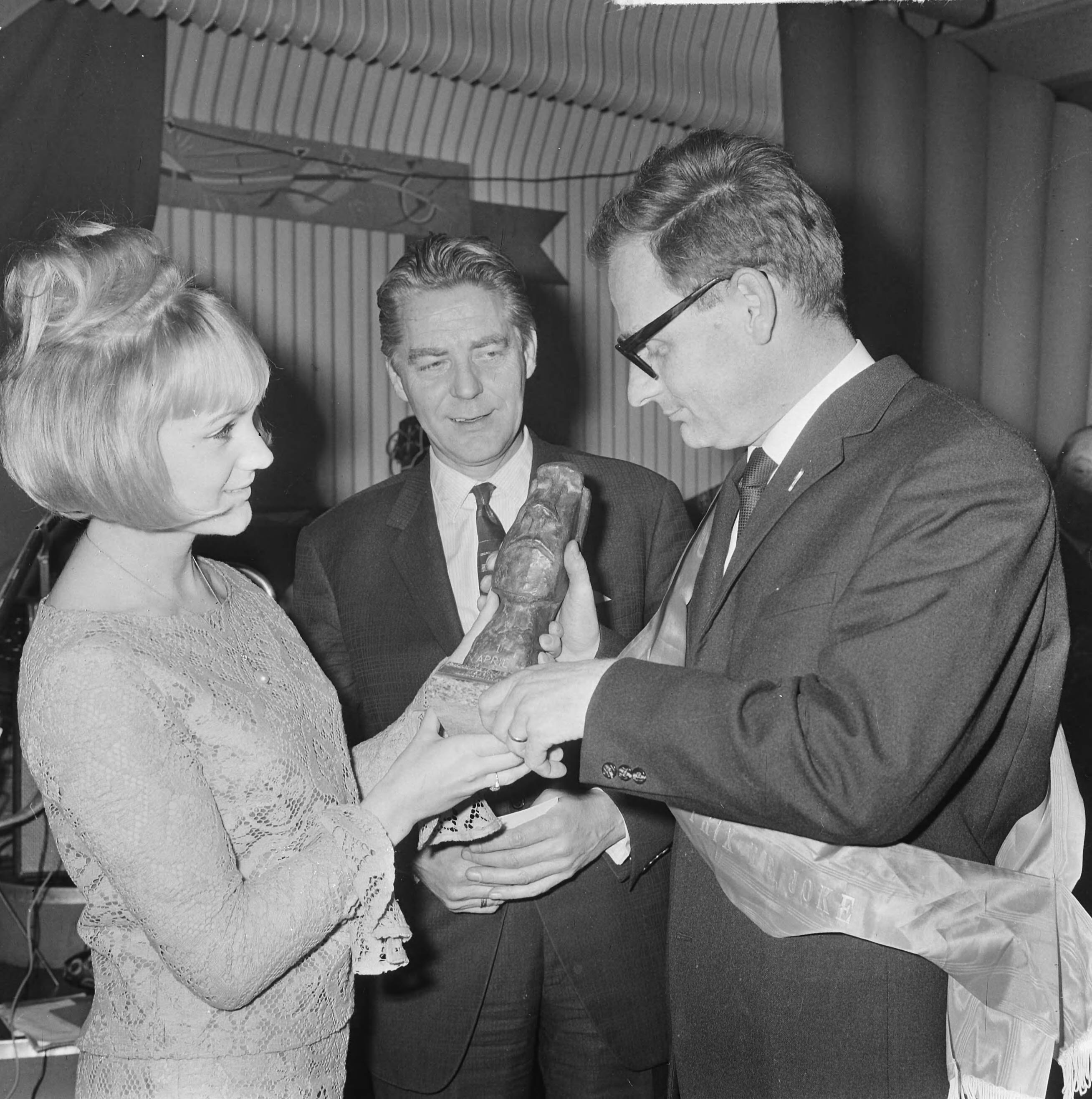 Fotocollectie Anefo — Uitreiking Prix de Joke 1965 aan Wijnand J. Maat in Hotel Bouwes te Zandvoort. Miss Zandvoort (Anneke Geerts) overhandigde de prijs, in het midden Bert Haanstra, de winnaar van vorig jaar — Foto: Koch, Eric / Anefo. Licentie: Set B: Rechtenvrij / Publiek Domein. Bron: Nationaal Archief. http://hdl.handle.net/10648/aa9ce4bc-d0b4-102d-bcf8-003048976d84